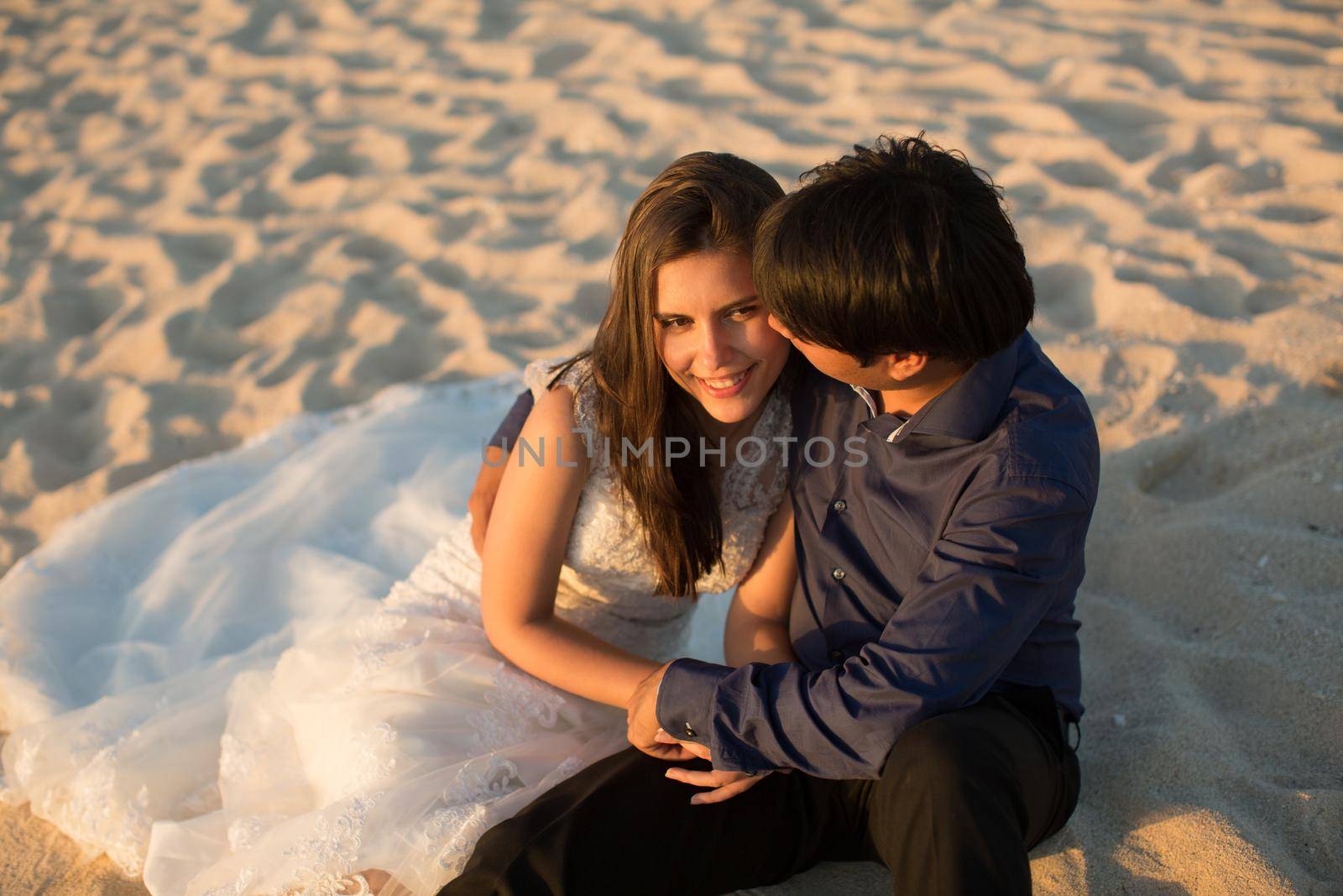 bride and groom sit on the sand