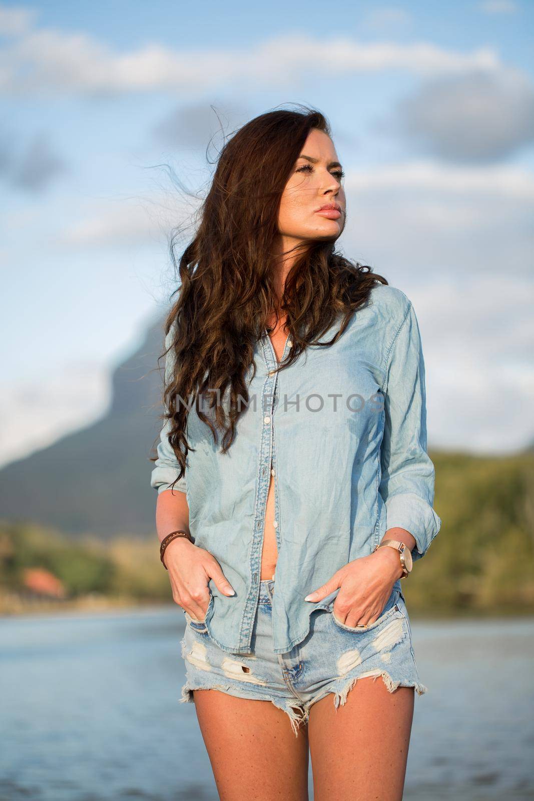 Young girl traveler stands on the beach against the mountain and enjoy the beauty of the sea landscape. Young girl loves wild life, travel, freedom.