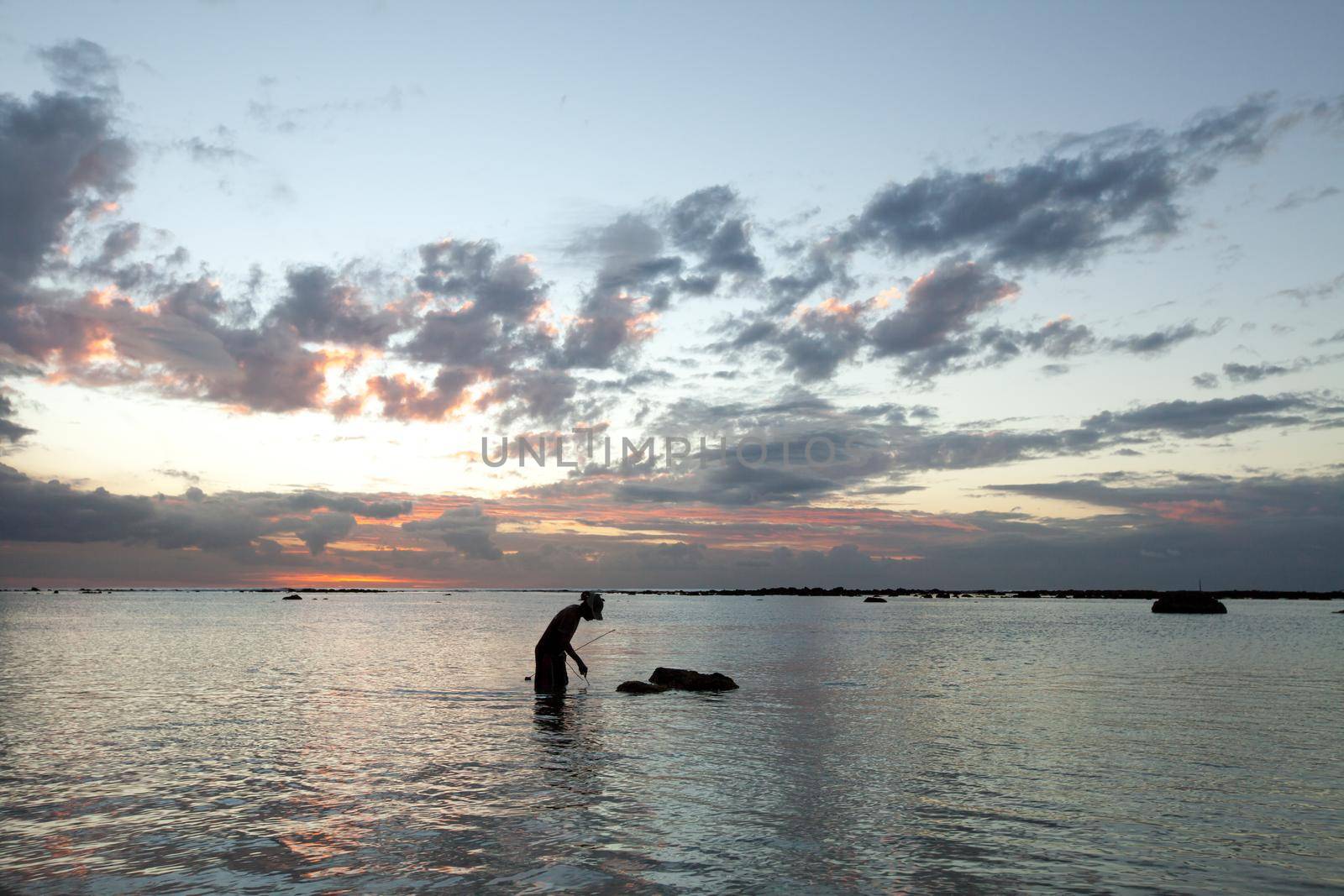 A fisherman catches a fish in the ocean at sunset by StudioPeace