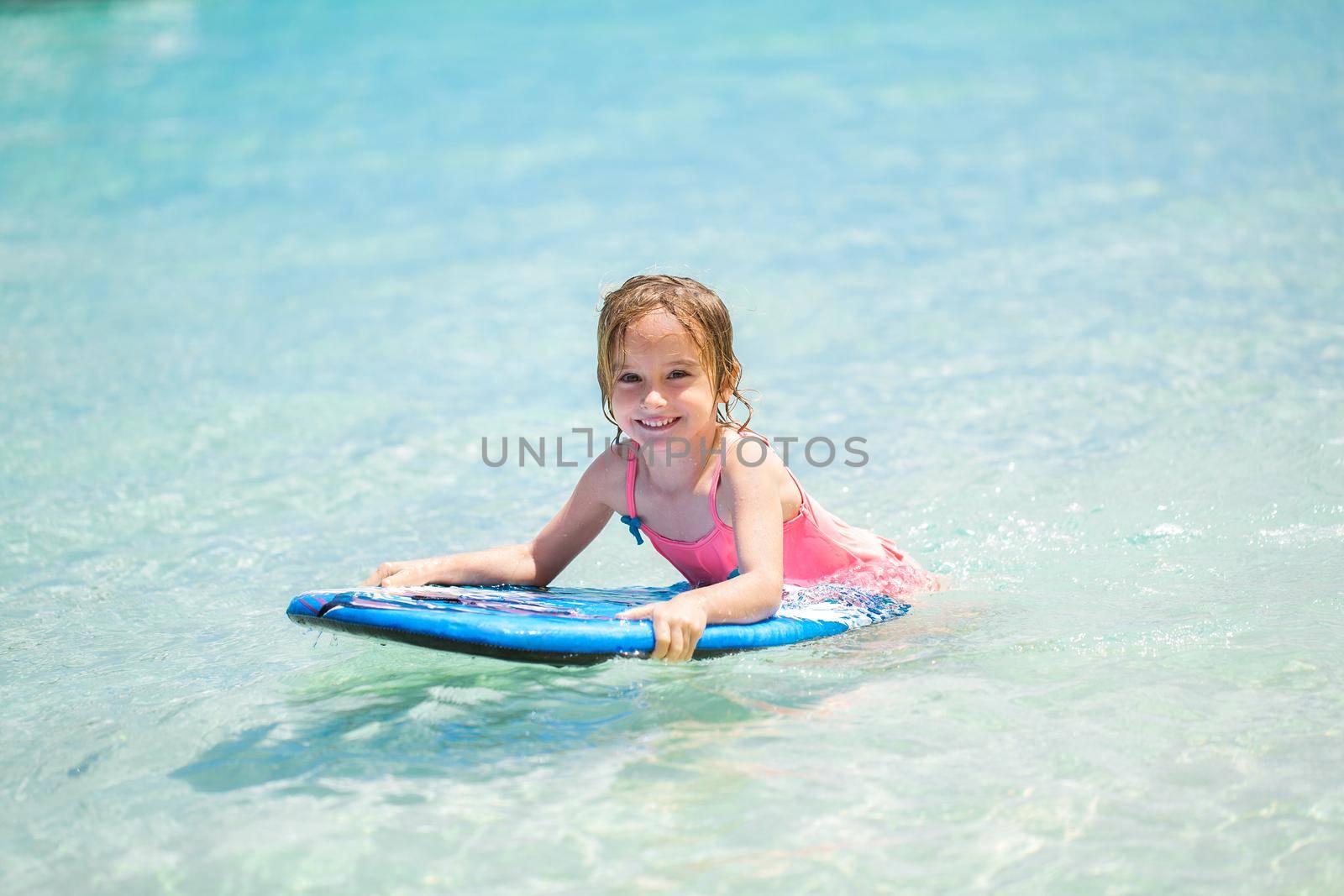 Little baby girl - young surfer with bodyboard has a fun on small ocean waves. Active family lifestyle