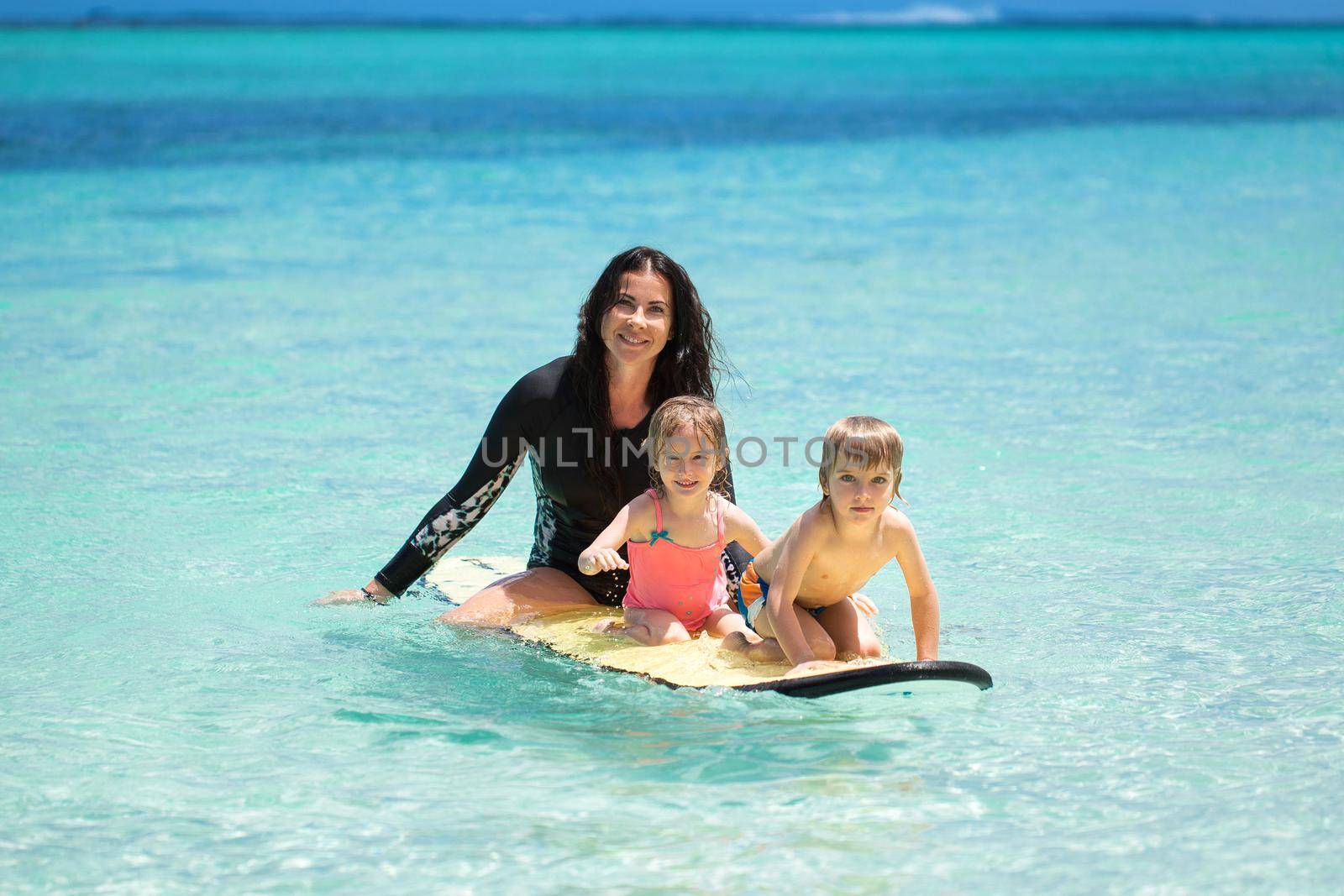 Twins, boy and girl with mom surfing in the ocean on a blackboard