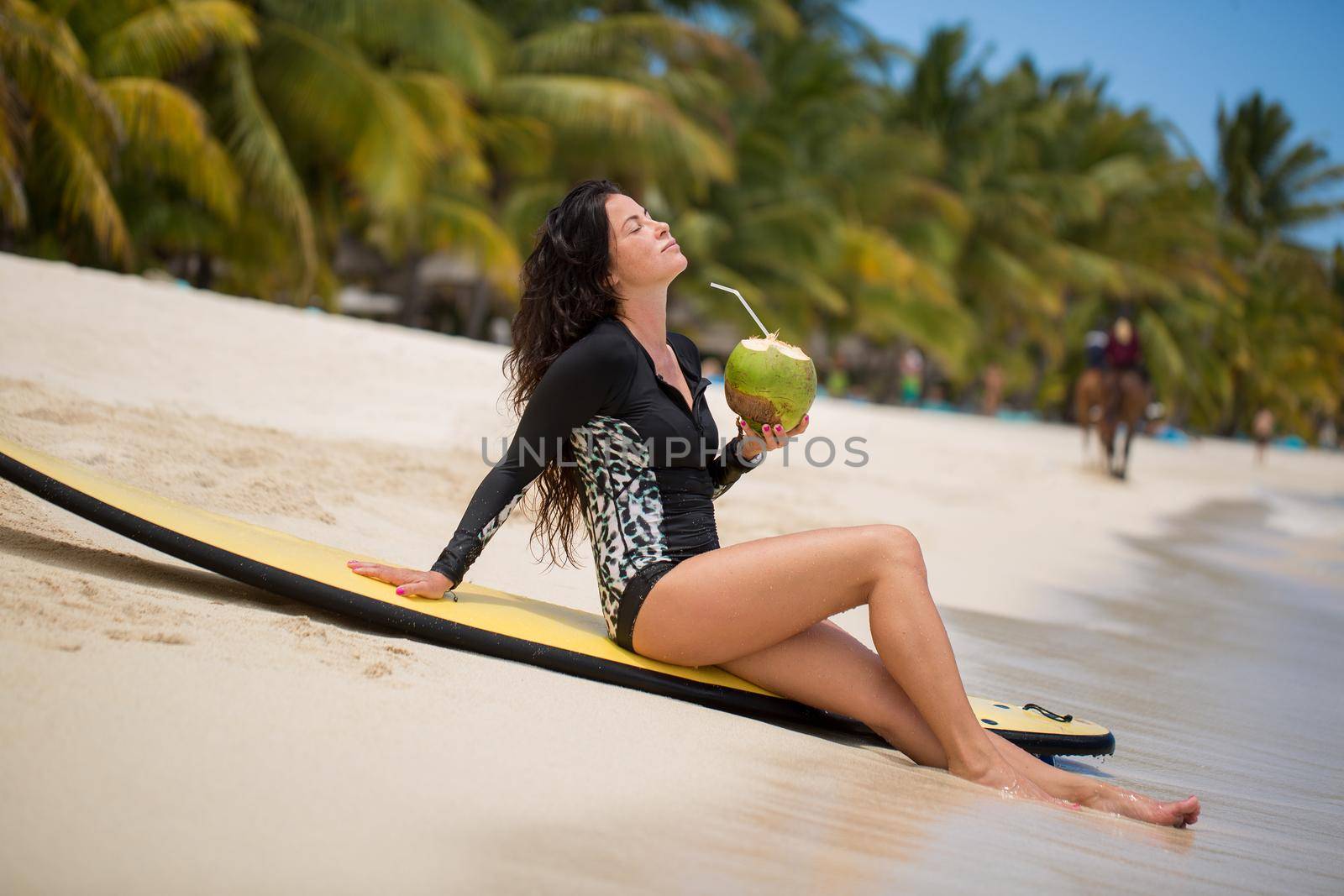 Portrait of a beautiful surfing girl with green coconut from palm tree sit on yellow surf longboard surfboard board. by StudioPeace