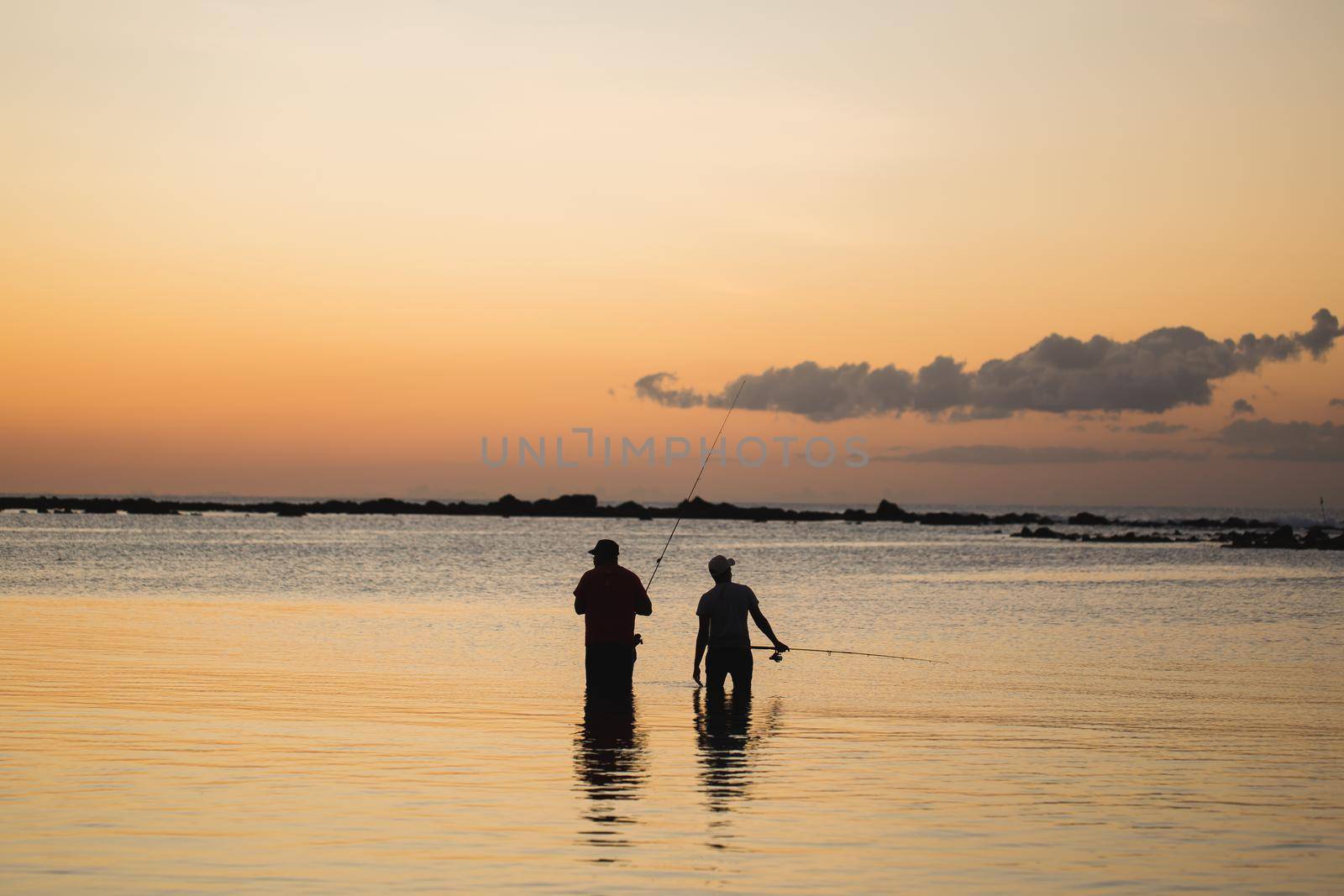 Two men fishing in the ocean from the beach at sunset. by StudioPeace