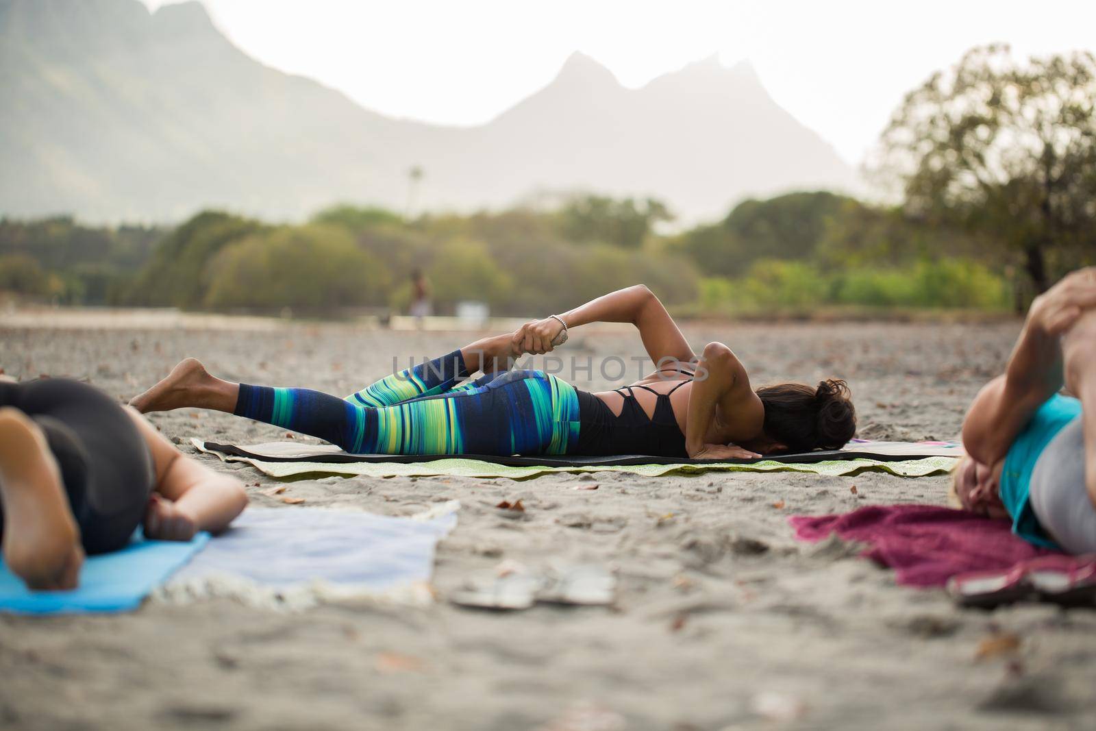 Women doing yoga exercises or supported pigeon pose on the background mountain on the empty beach of the Indian ocean in Mauritius. by StudioPeace