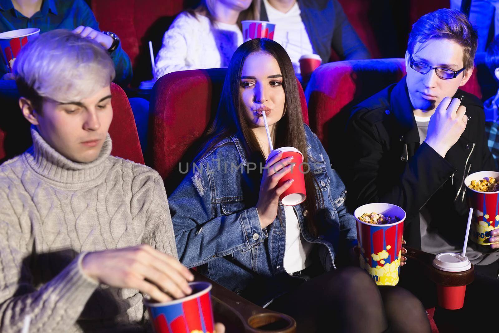 Cheerful company in the cinema. A girl drinks from a glass, a man eats popcorn.