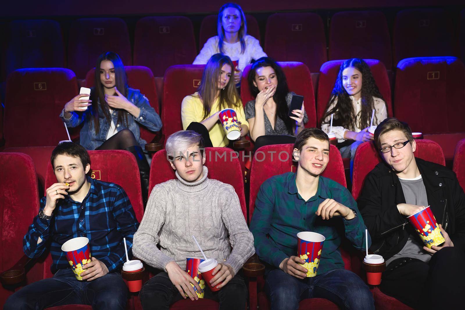 Friends sit in a cinema watch film eating popcorn and drinking aerated sweet water. Movies and entertainment concept. by StudioPeace