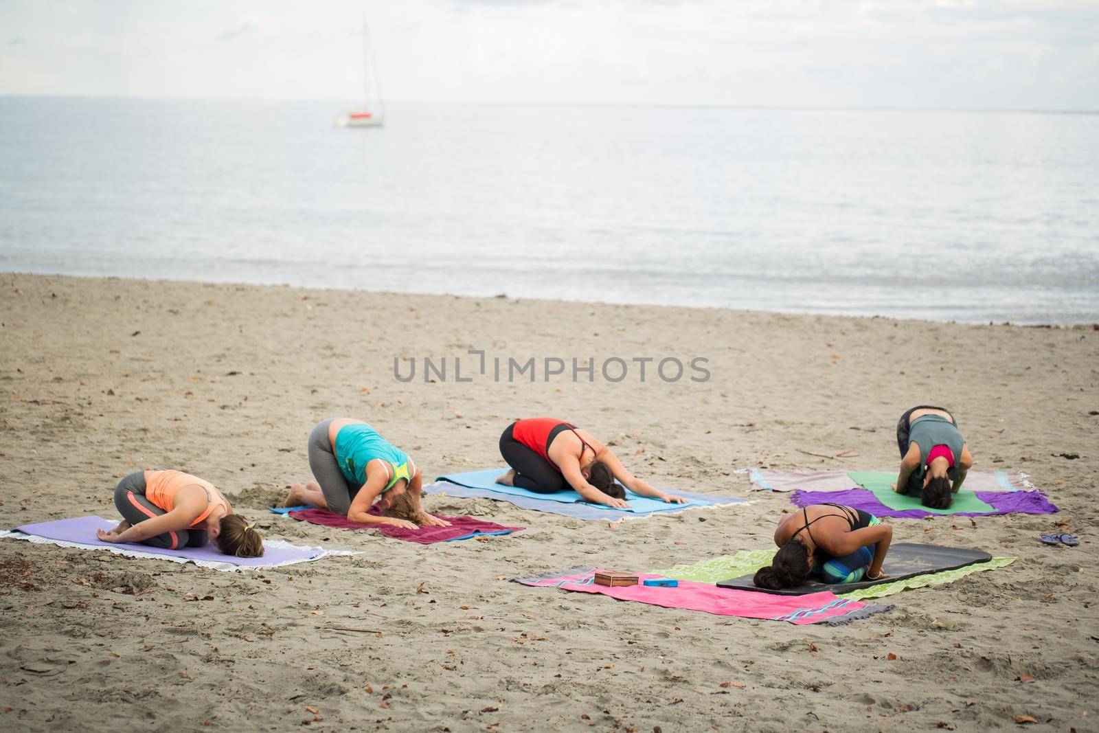 Women doing yoga exercises or supported pigeon pose on the background mountain on the empty beach of the Indian ocean in Mauritius. by StudioPeace