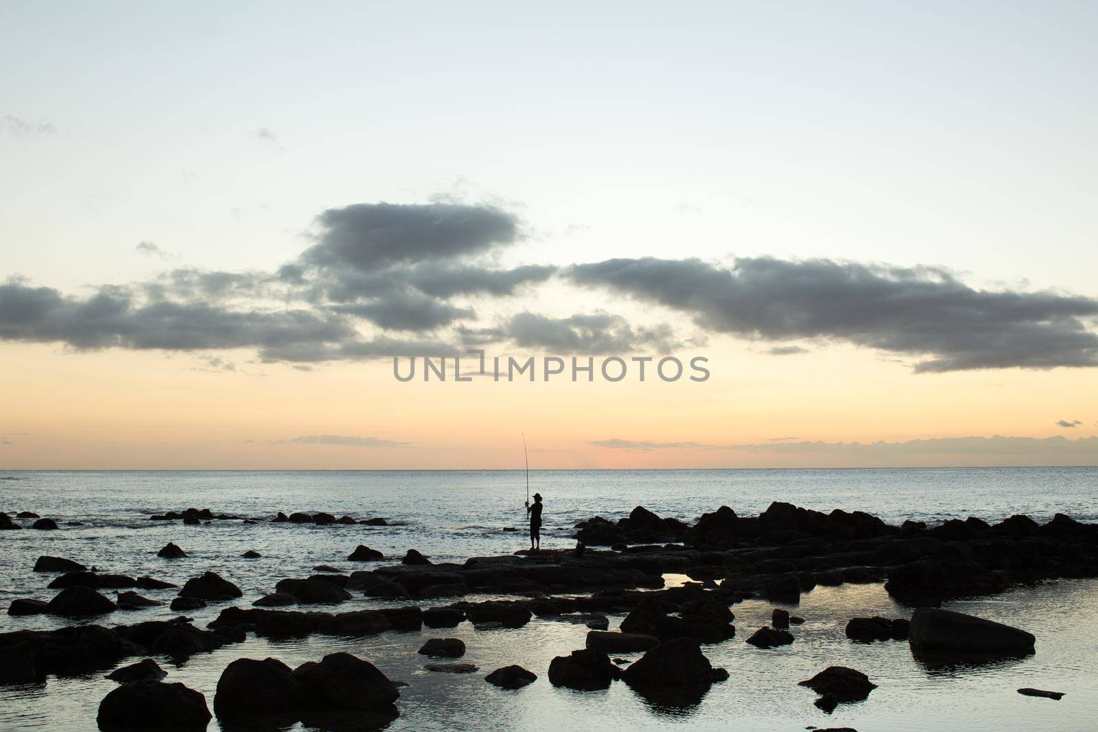 A fisherman is fishing in the black stones in the ocean.