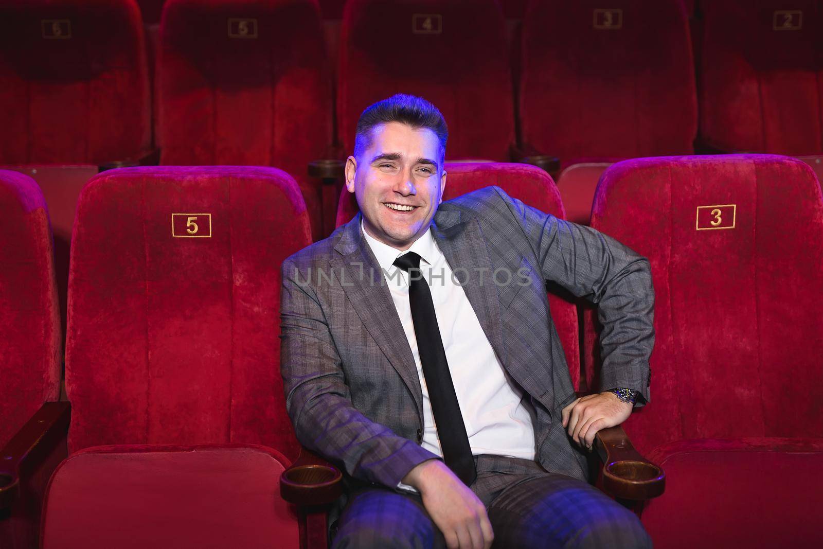 Portrait of a young handsome man alone in a movie theater in a business suit