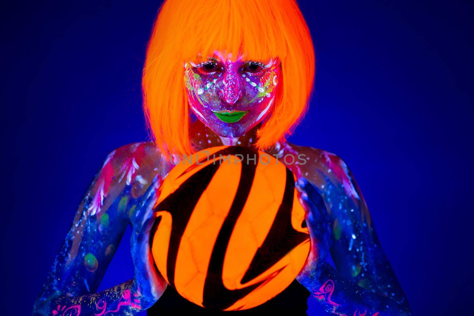 Woman in neon makeup holds a soccer ball in her hands. Concept of the world Cup. Fluorescent paint in UV light. by StudioPeace