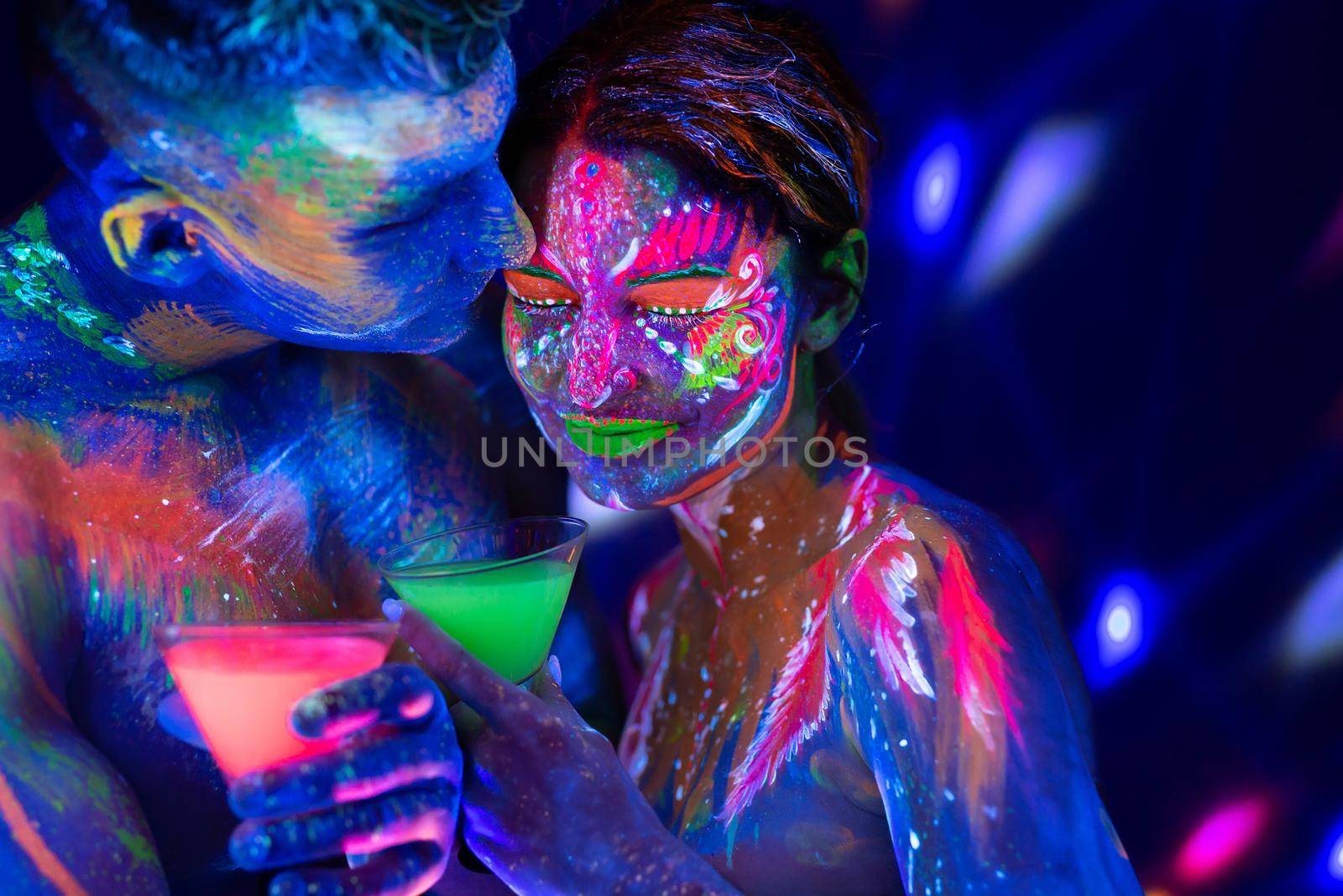 Young couple drink an alcoholic drink in a nightclub. Man and woman with fluorescent bodyart