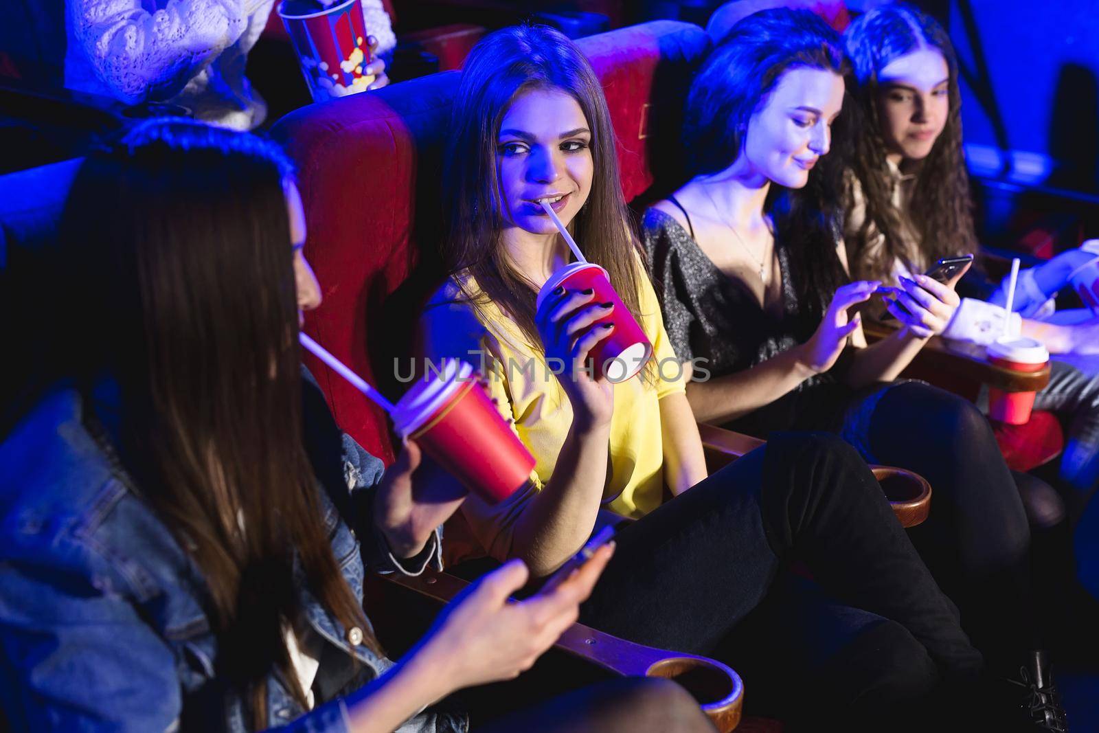 Young beautiful women drink from a glass in the cinema and watch a movie by StudioPeace