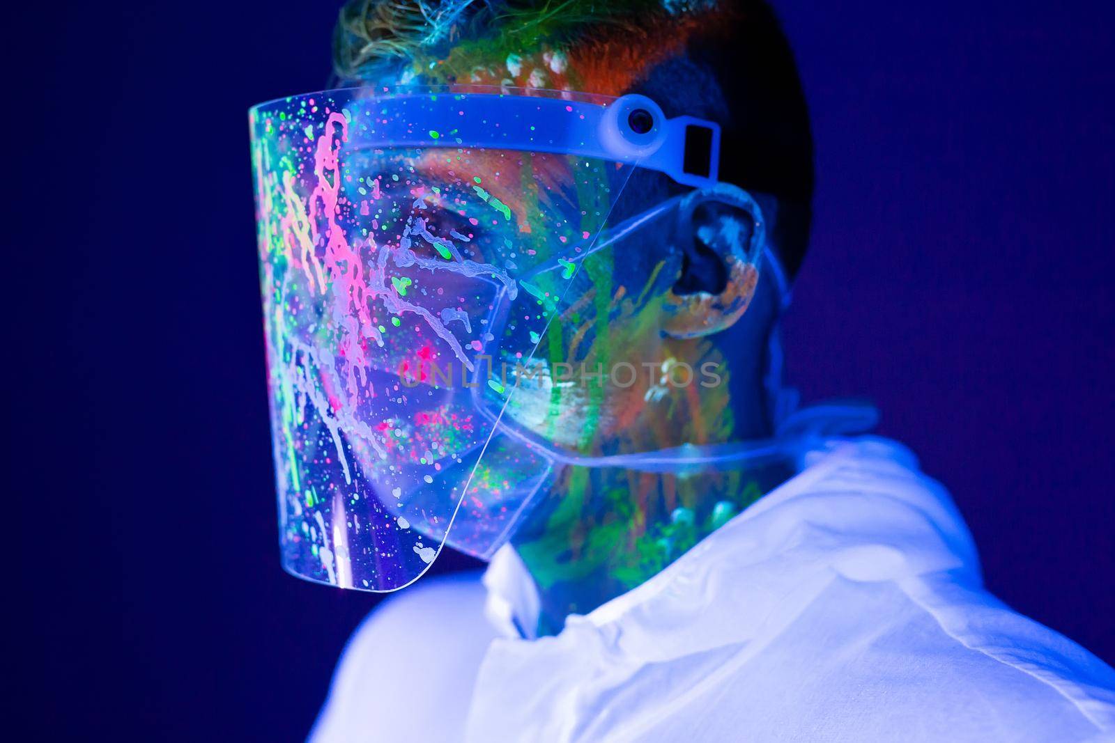 Portrait of man doctor in protective clothes in ultraviolet neon light during coronavirus pandemic. Epidemic, pandemic of coronavirus covid-19. by StudioPeace