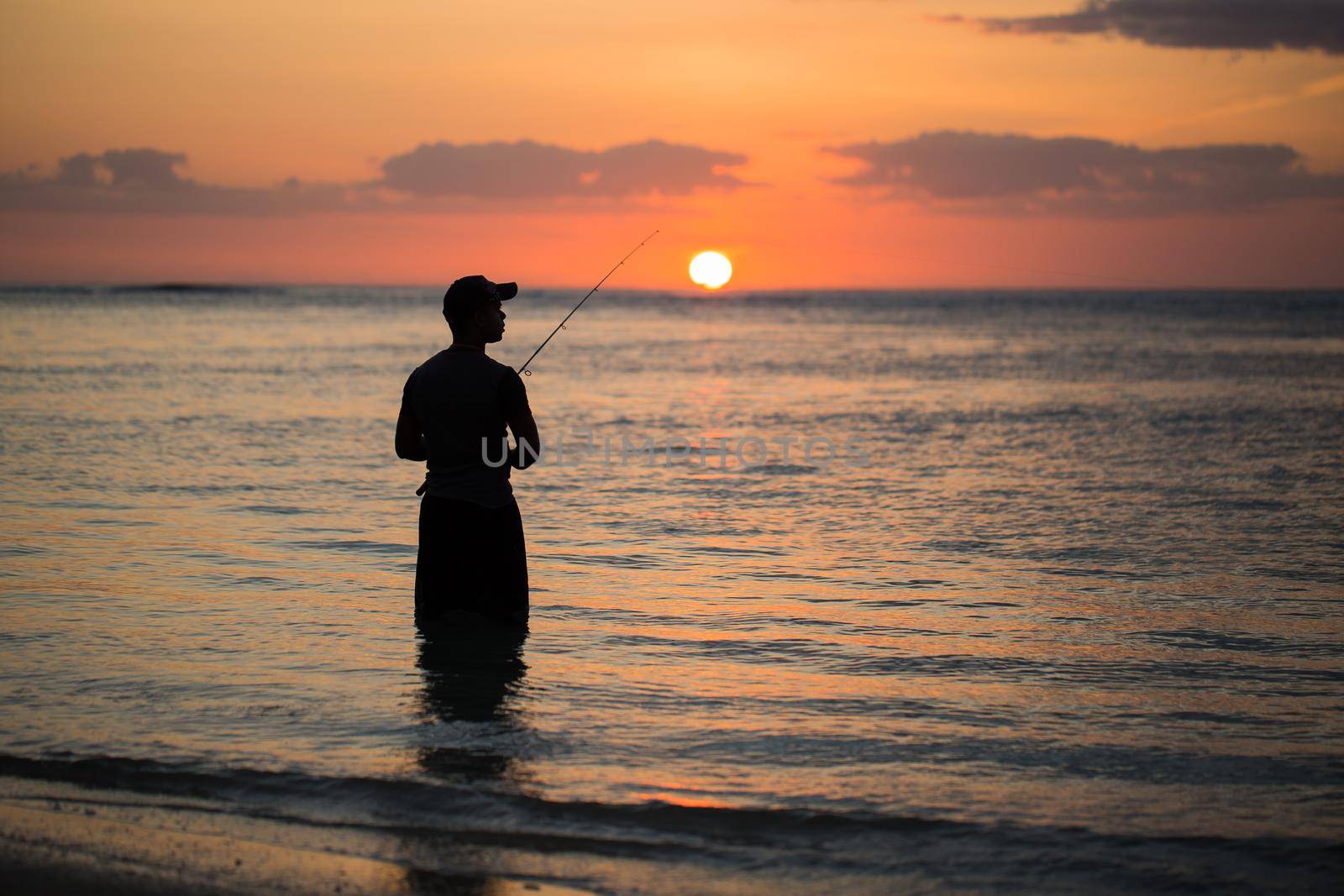 A man fishing in the Indian ocean with the beach at sunset. by StudioPeace