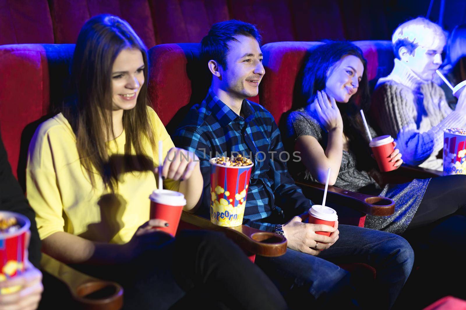 Friends sit and eat popcorn together while watching movies in a movie theater. by StudioPeace