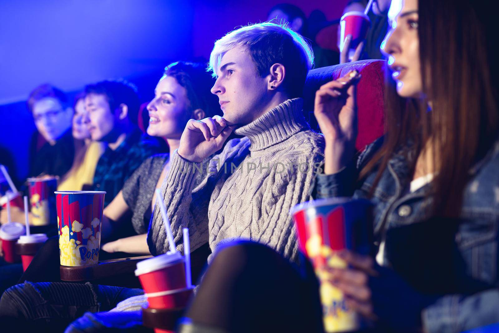 Friends sit and eat popcorn together while watching movies in a movie theater. by StudioPeace