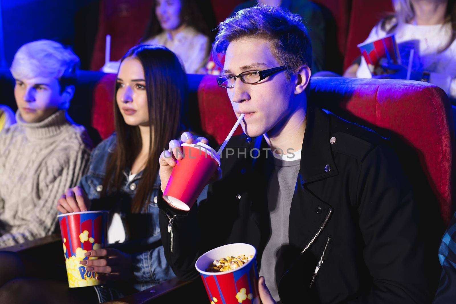 Young man drinks from a red Cup in the cinema.