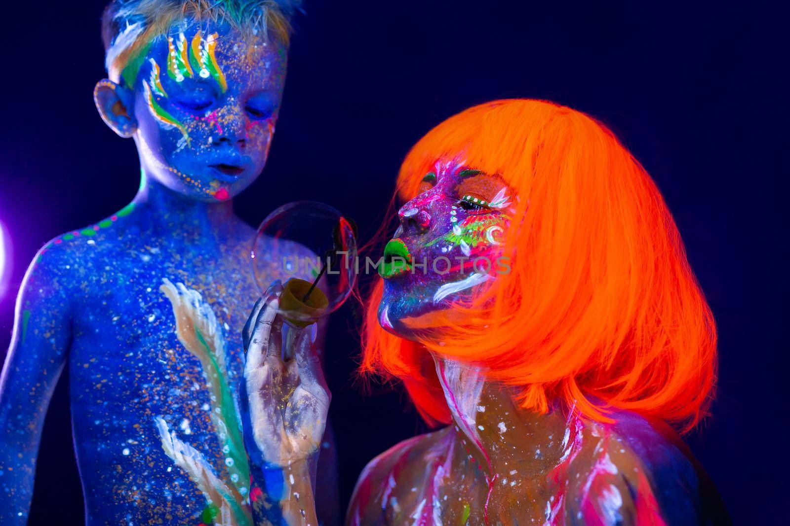 Young mother and son play with soap bubbles. Painted with fluorescent paint using UV light. by StudioPeace