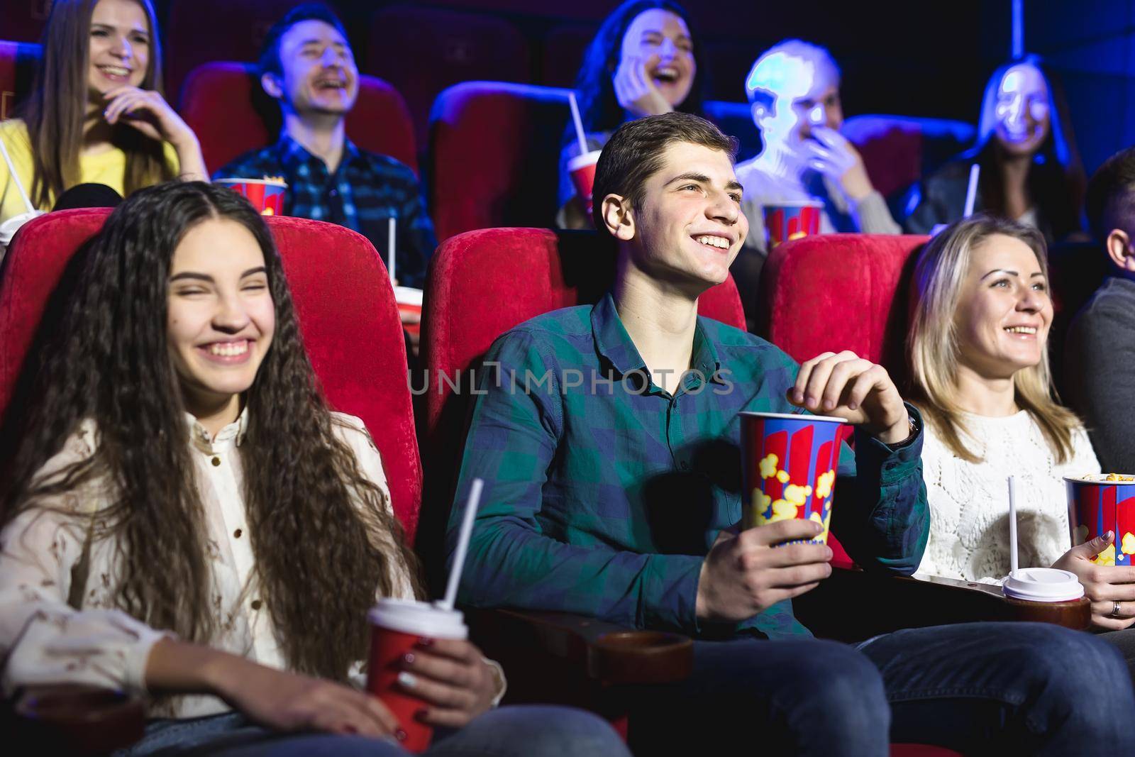 Friends sit and eat popcorn together while watching movies in a movie theater. by StudioPeace
