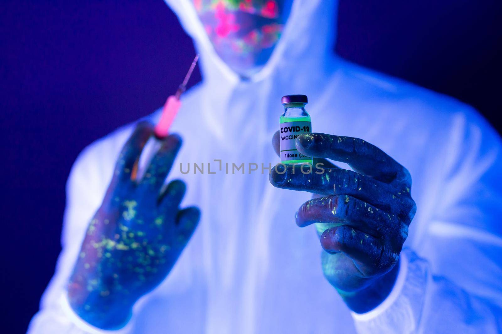 Doctor in ultraviolet neon light is holding COVID-19, oronavirus vaccine and syringe using for prevent infection. Medicine and Healthcare concept. by StudioPeace