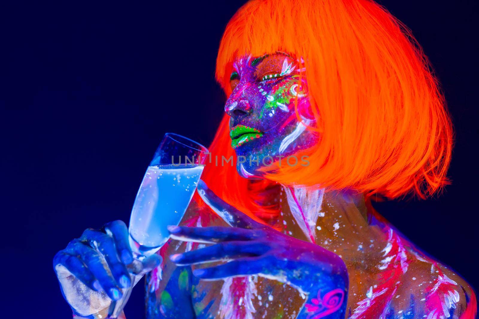 Woman drinking champagne in neon light, disco night club. Beautiful dancer model girl colorful bright fluorescent makeup