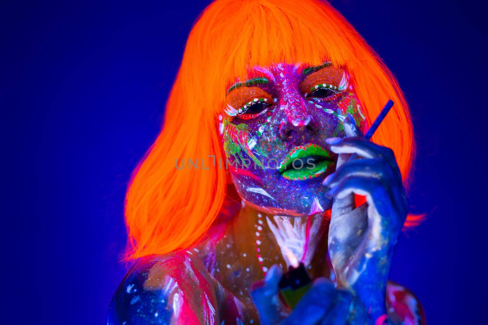 Woman with a cigarette in neon light. Beautiful model girl colorful bright fluorescent makeup. Dangers of smoking