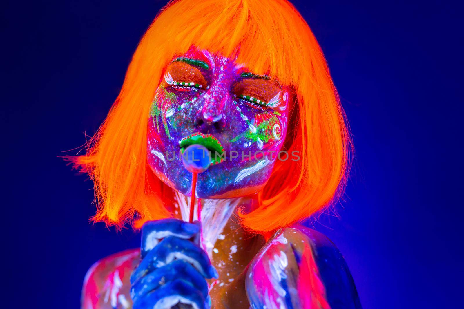 Fashion model woman licks sweet candy in neon light, disco night club. Beautiful model girl colorful bright fluorescent makeup