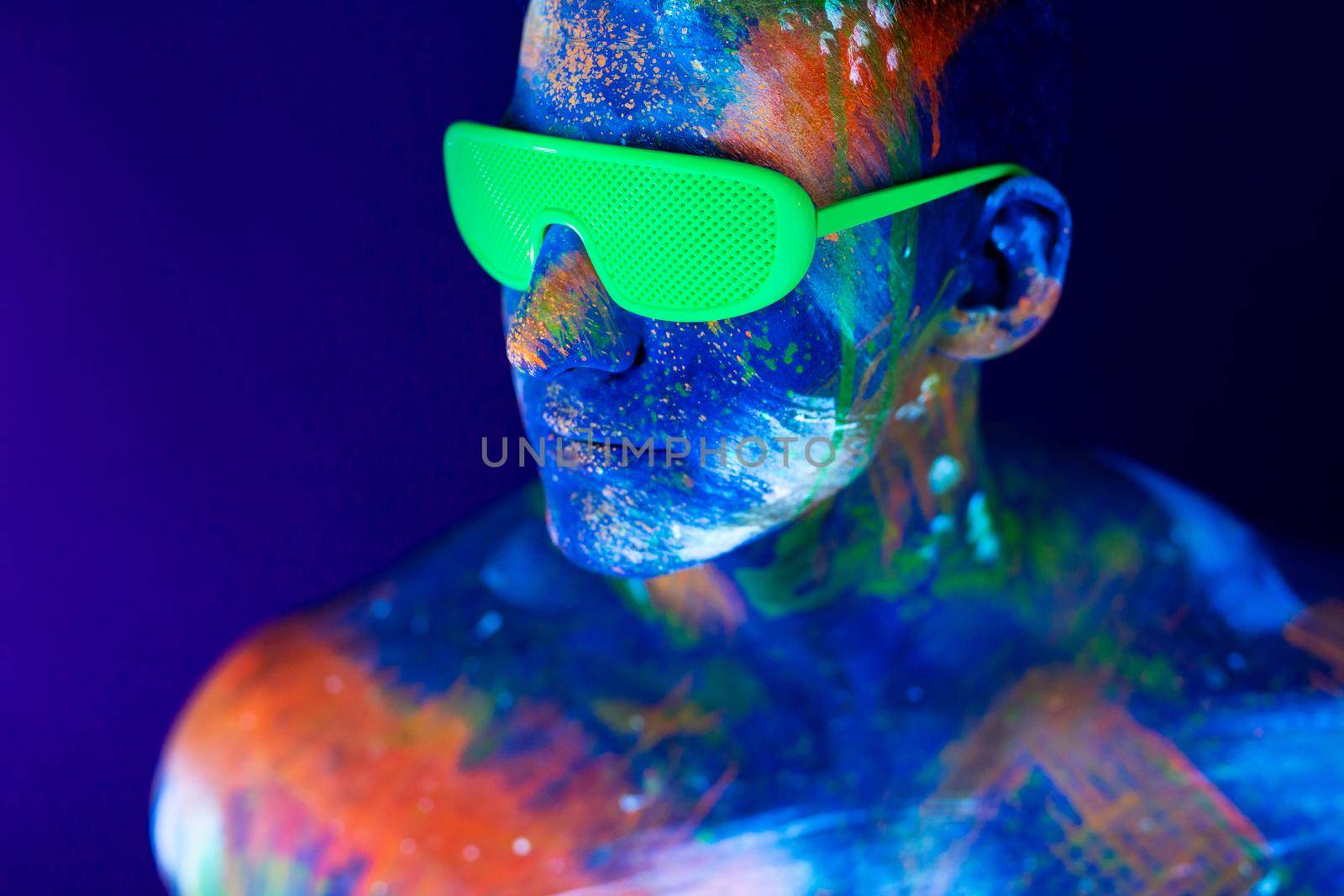 Young man shouts. Fluorescent paint on face and muscular torso, in studio shot with UV light