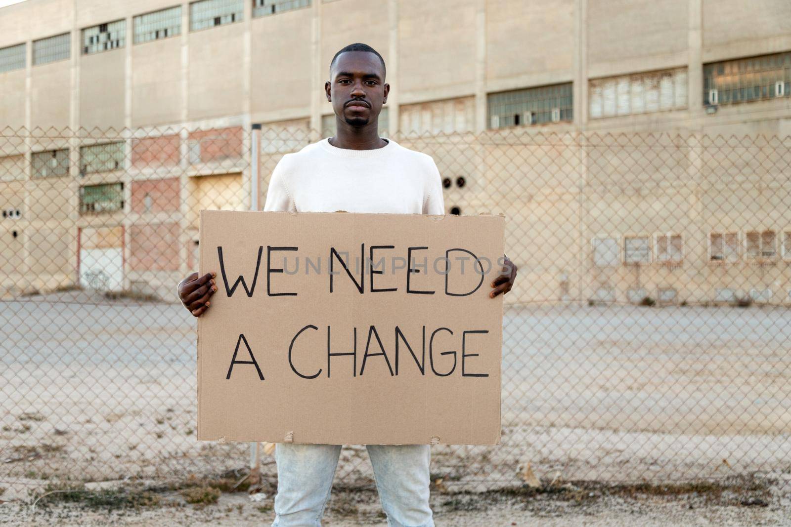 Young African American man looking at camera holds we need a change banner protest for black lives matter. Copy space. by Hoverstock