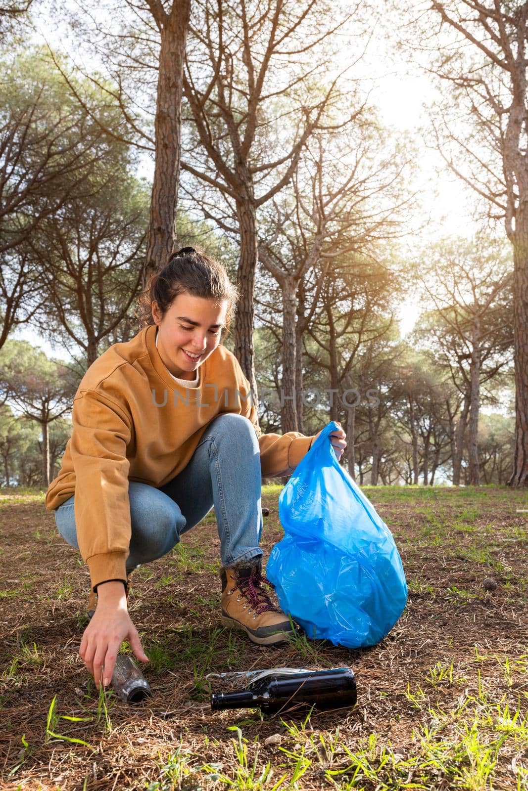 Happy young caucasian woman picking up plastic bottle cleaning forest. Copy space. Vertical image. Ecology concept.