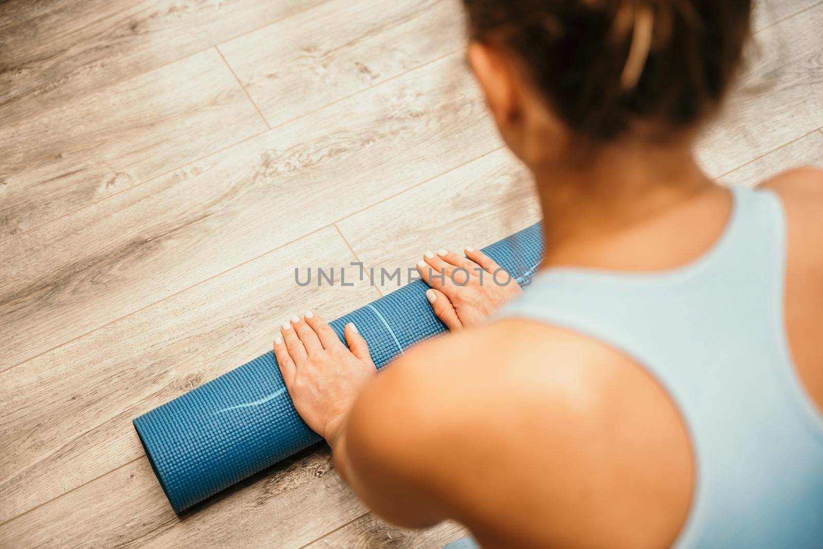 Woman hands rolled up yoga mat on gym floor in yoga fitness training room. Home workout woman close up hands rolling foam yoga gym mat. Woman barefoot home workout sportive healthy lifestyle concept by Matiunina