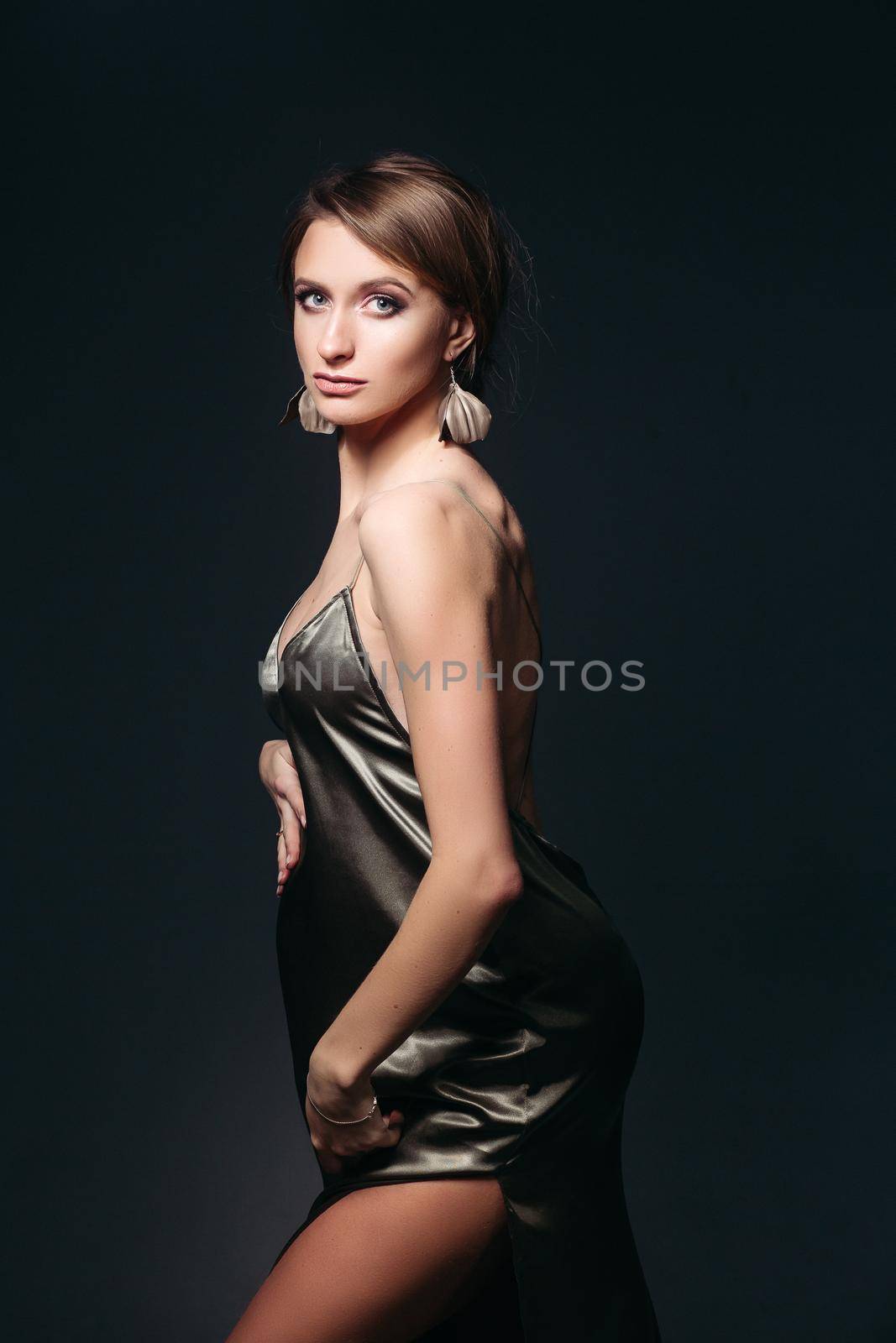 Studio portrait of sensual and beautiful pregnant woman in sexy silk dress, embracing belly. Elegant and stylish female posing, looking at side. Concept of pragnancy fashion and look.
