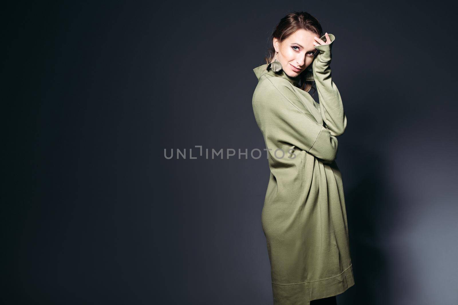Elegant and fashionable pregnant woman posing at dark studio, sensuality touching face by hands. Stylish woman wearing in khaki dress with pregnant belly, looking at camera. Concept of pregnancy.