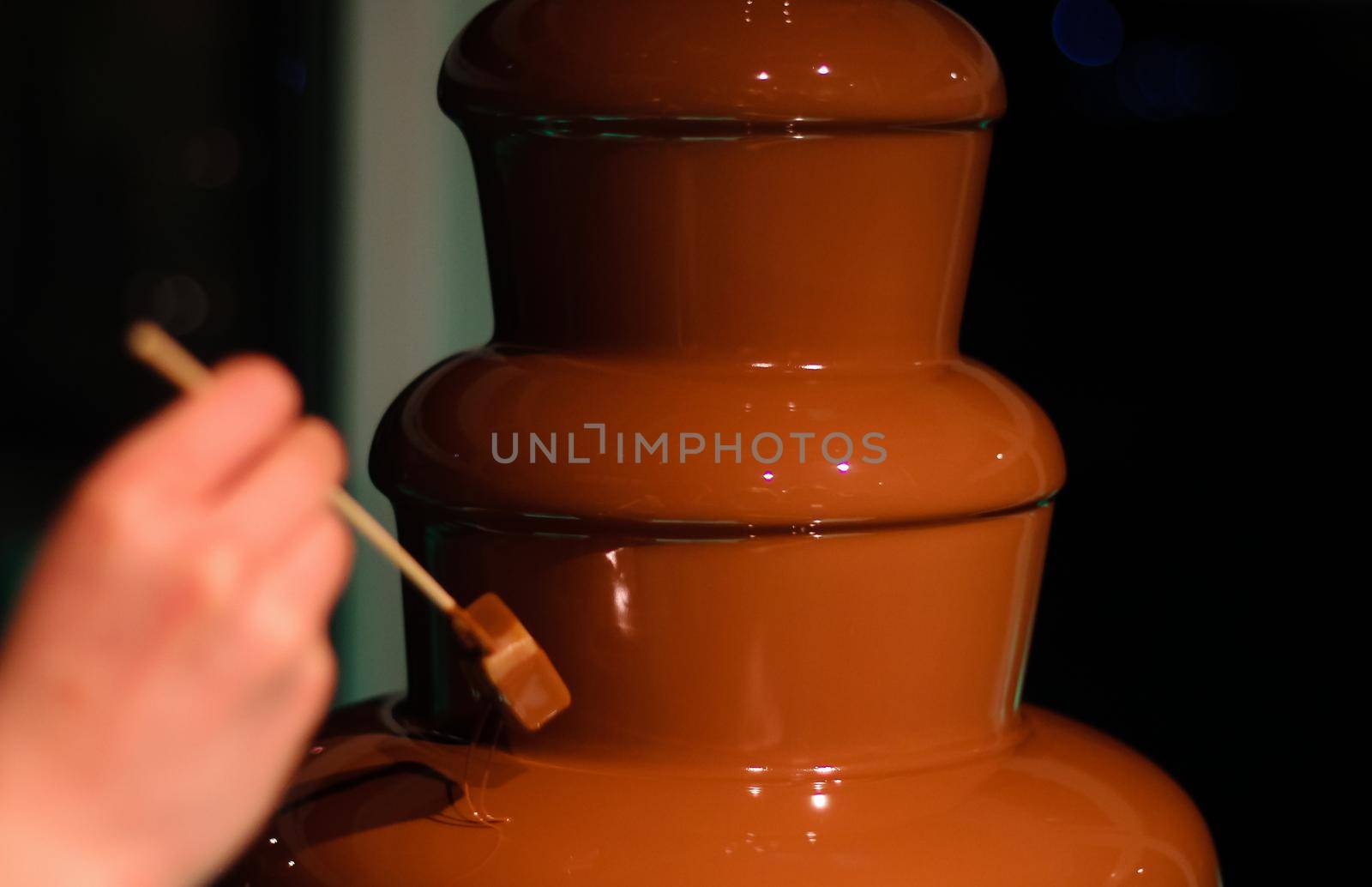 Person dipping a block of British fudge on a skewer into a chocolate fountain fondue, at a wedding in Hampshire, UK. High quality photo.