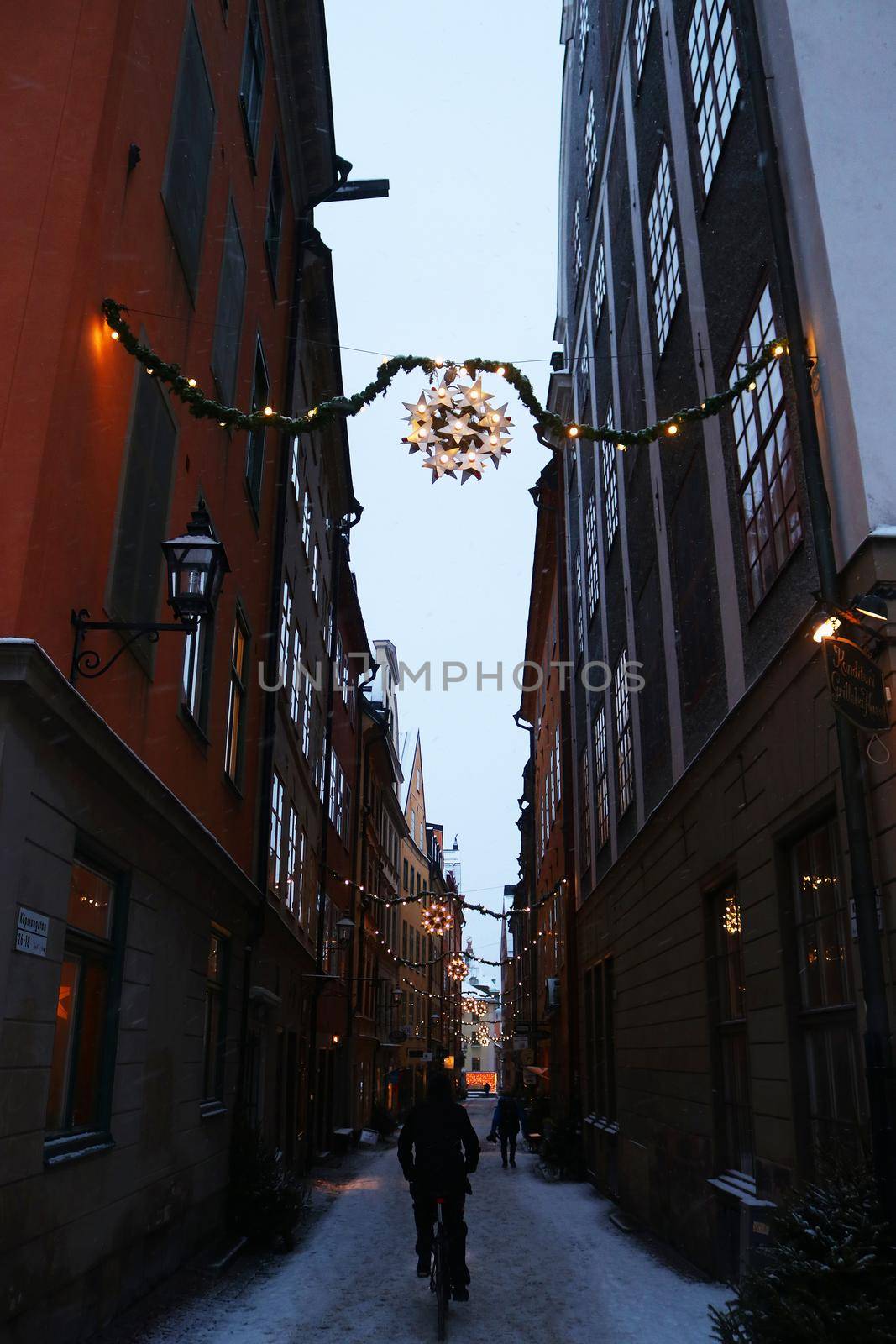 Christmas decorations, cyclist and lights in a snowy street in the centre of Stockholm, 'Gamla Stan' in winter, Sweden. High quality photo.