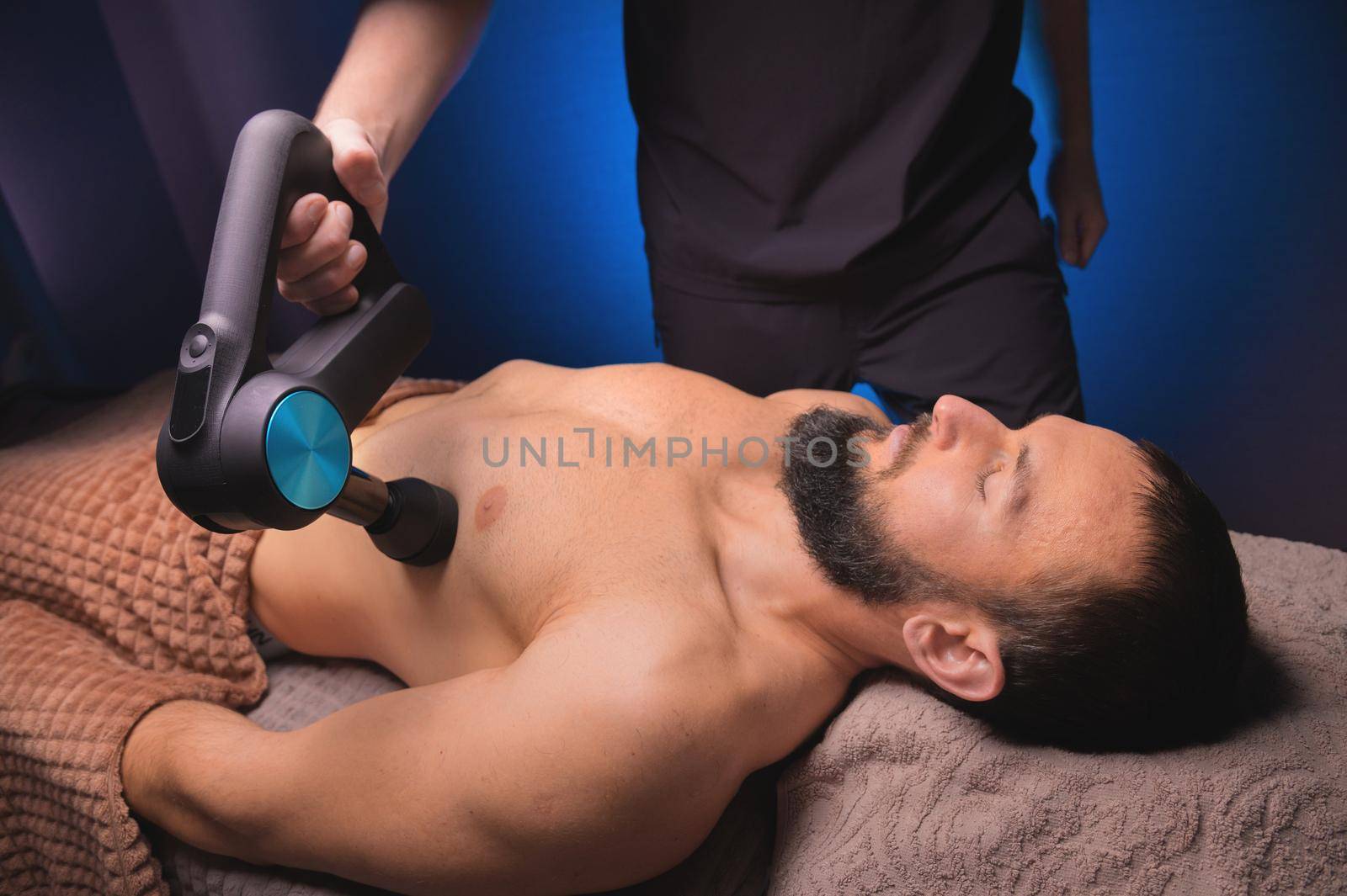 Close-up of a Caucasian male pectoral muscle percussion massager working out in a professional massage parlor.