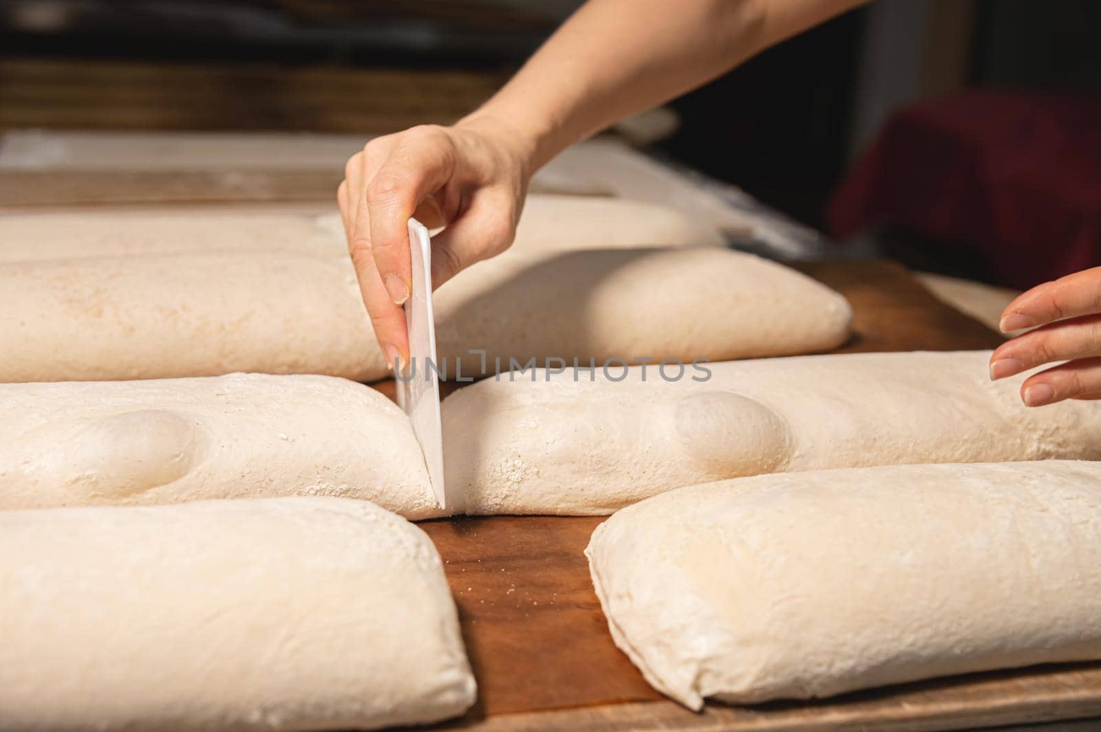 Close-up of a baker's female hands cutting a loaf of dough into a loaf of bread with a blade before baking in the oven. Craft craft bread production by yanik88