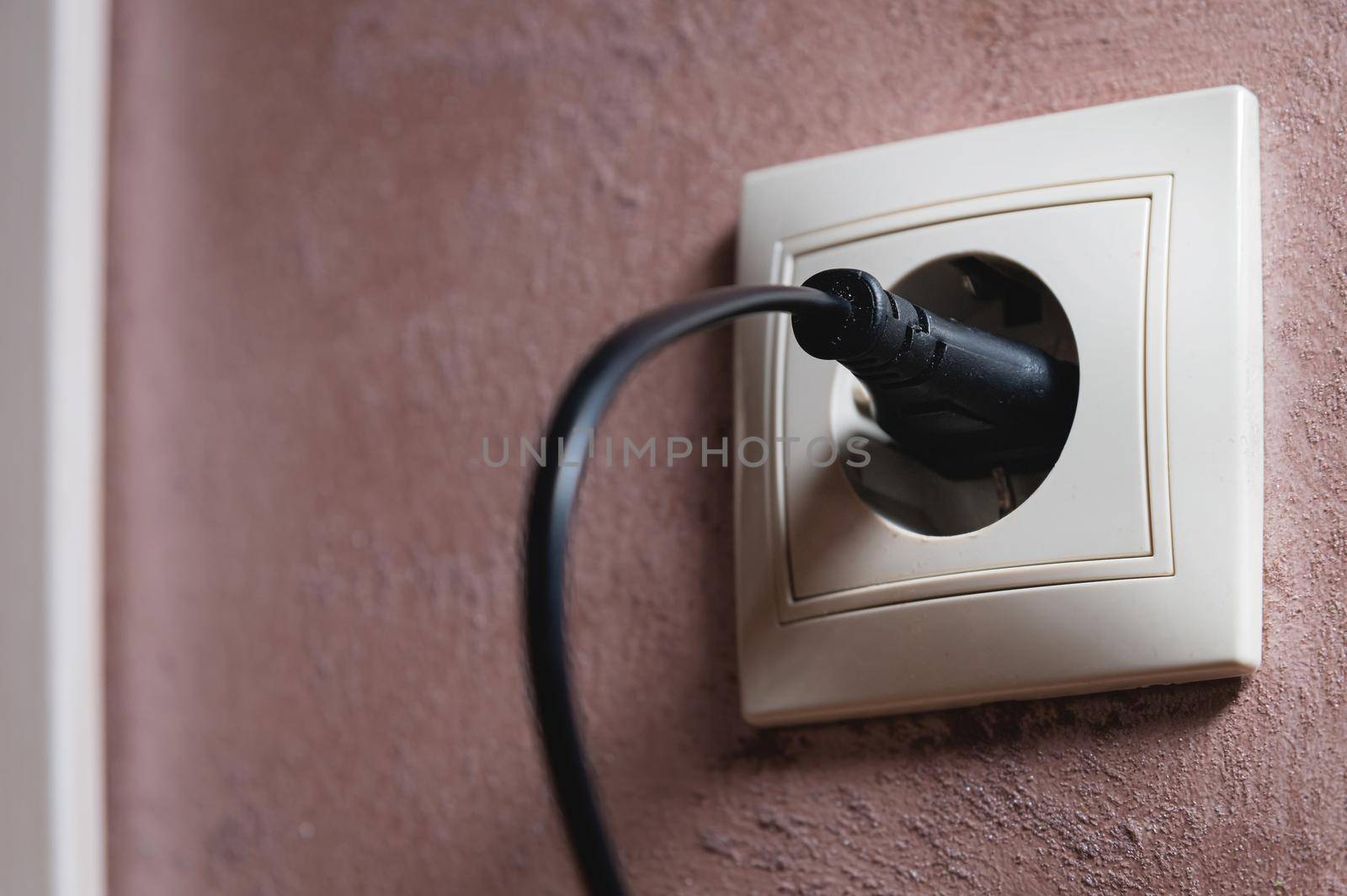 Close-up of a black electric plug in a 220 socket in the wall. Power on concept.