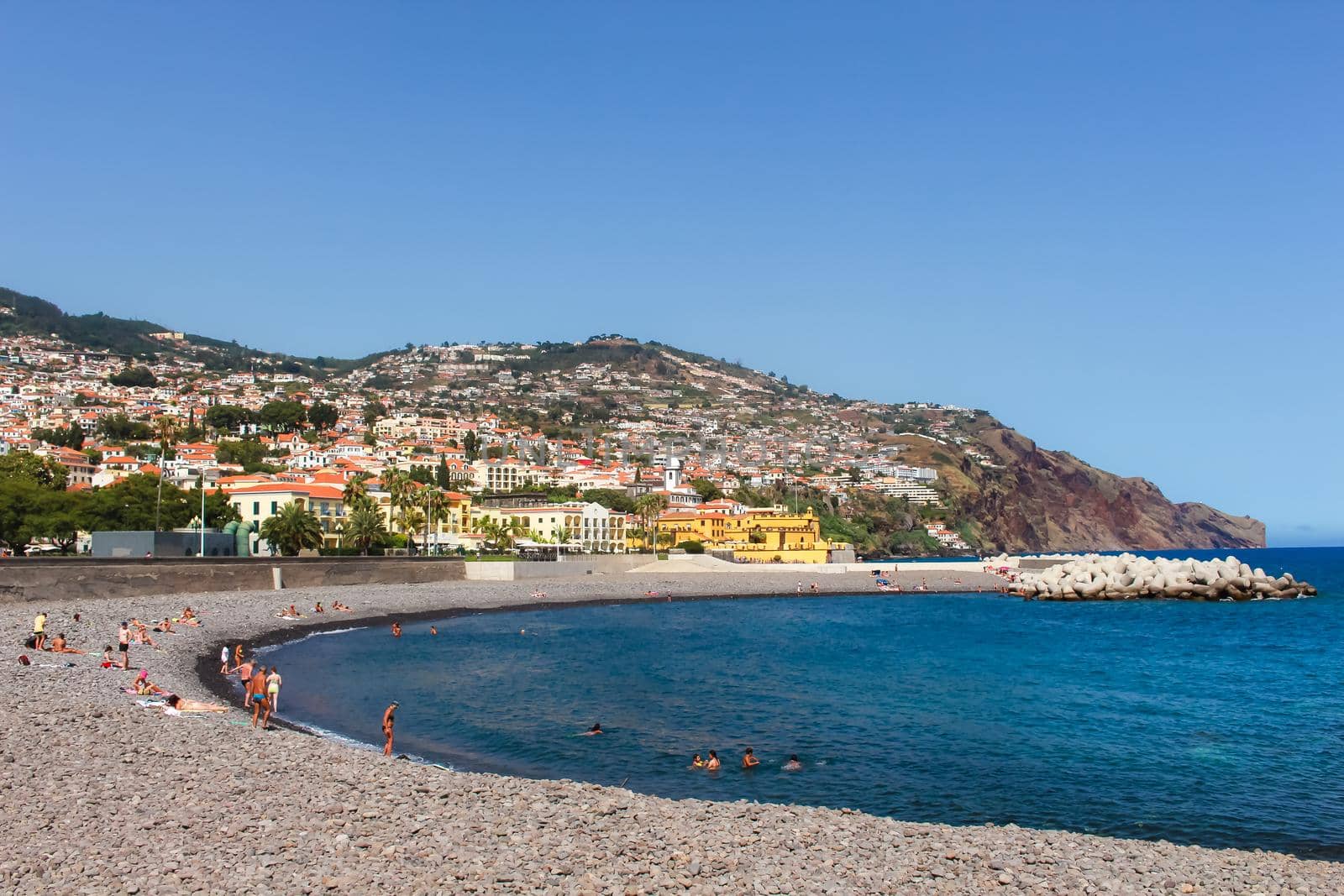 Sunbathers relaxing on the pebble beach coastline of vibrant Funchal, Madeira, Portugal.