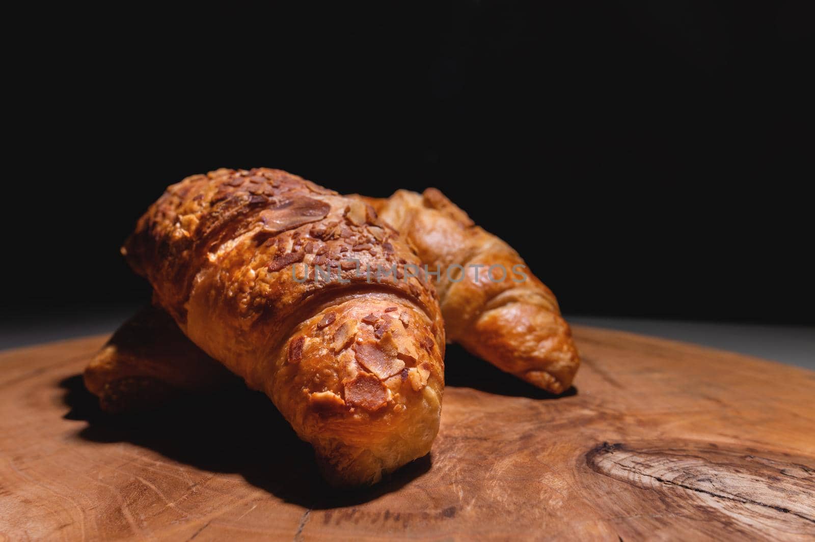 Several Croissants on a cutting board made of sawn wood on a dark background. Healthy and tasty breakfast.