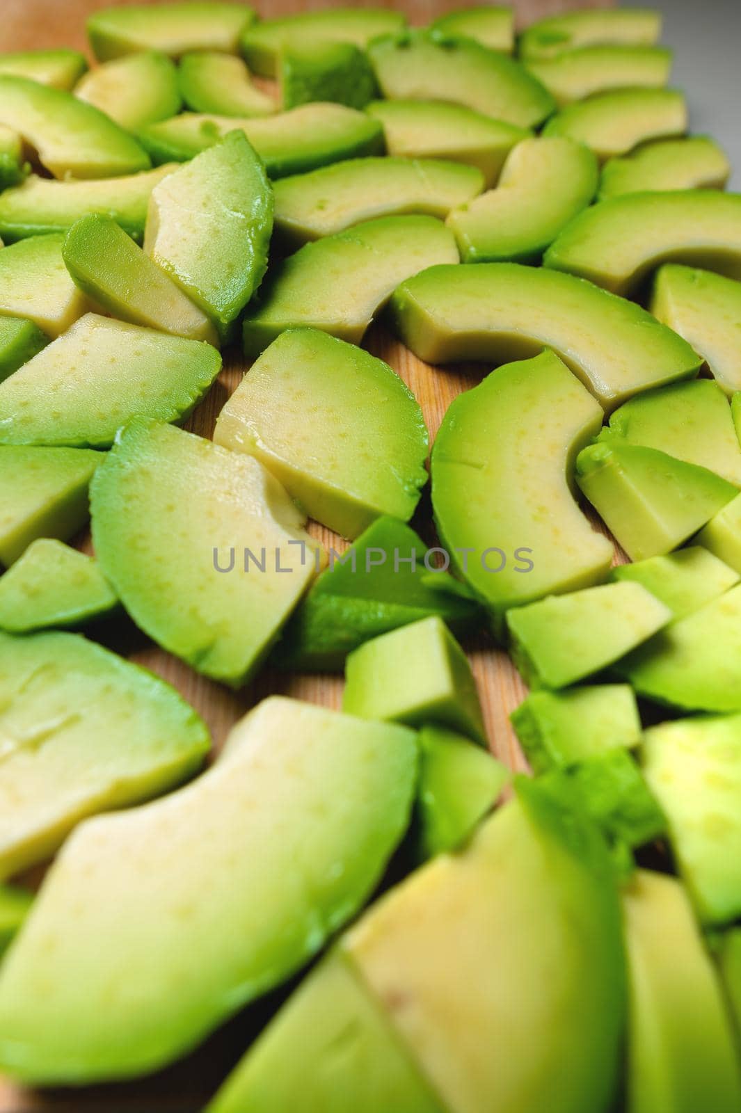 Pieces of juicy sliced avocado lie textured on a wooden cutting board. Delicious vegan background by yanik88