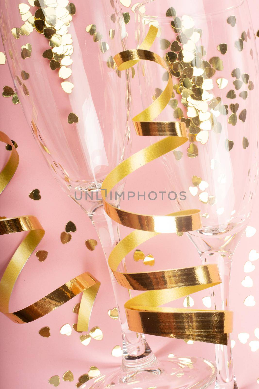 Valentines day champagne flutes glasses and heart shaped gold glitters on pink background