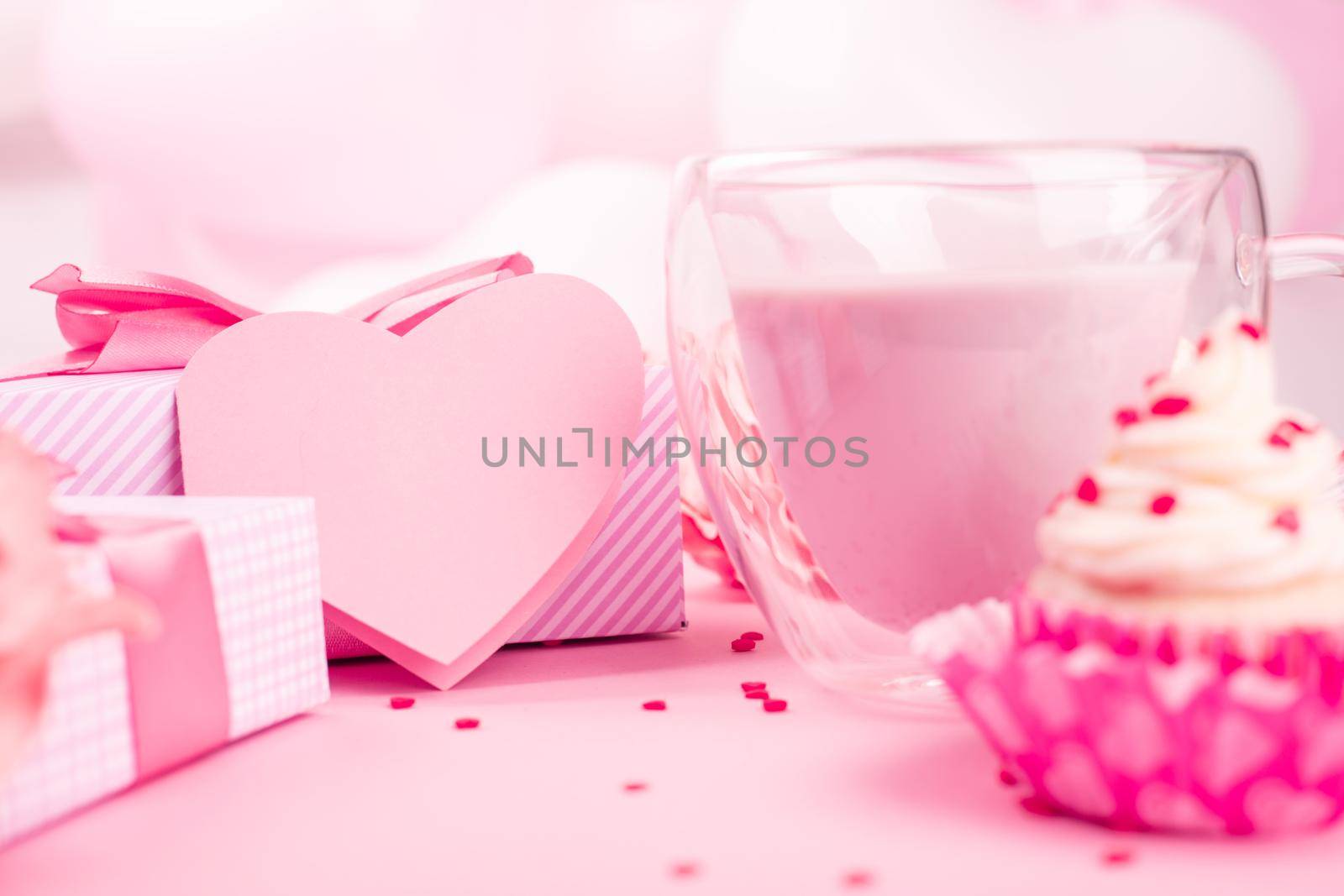 Valentine Day gift in a box wrapped in striped paper and tied with silk ribbon bow and dessert on pink balloons background with copy space for text