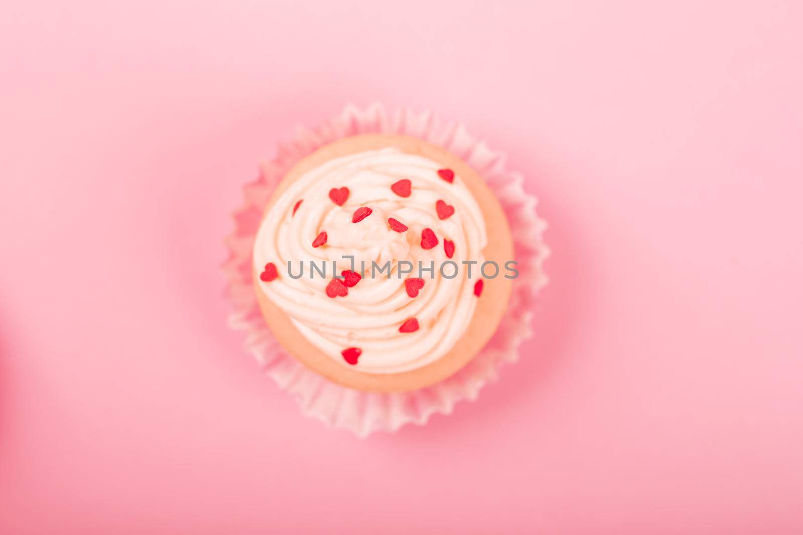 Valentine day love cupcake decorated with cream and hearts on pink background with copy space for text top view