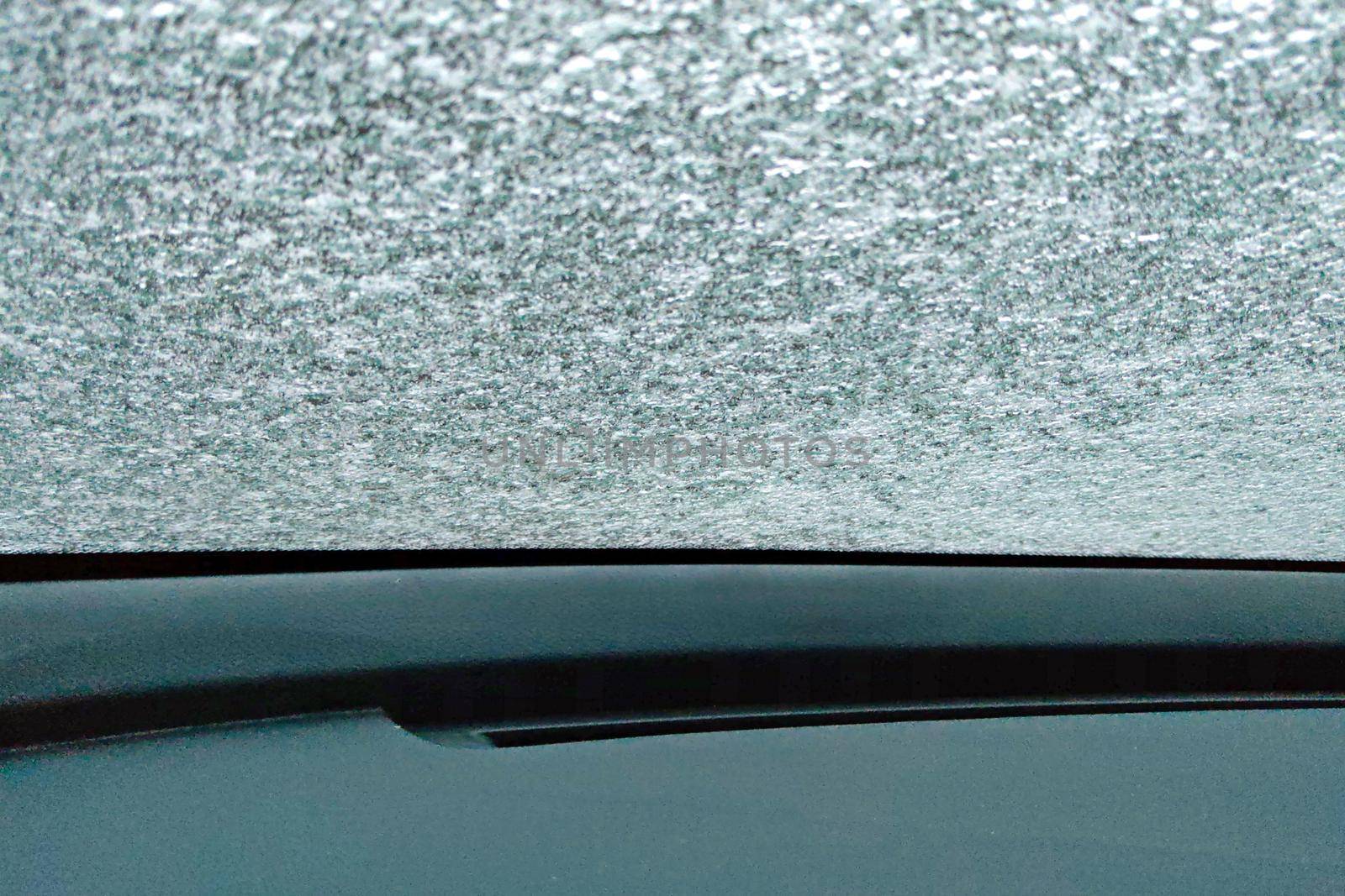 The glass of the car is covered with thin ice. Warming up the car in winter