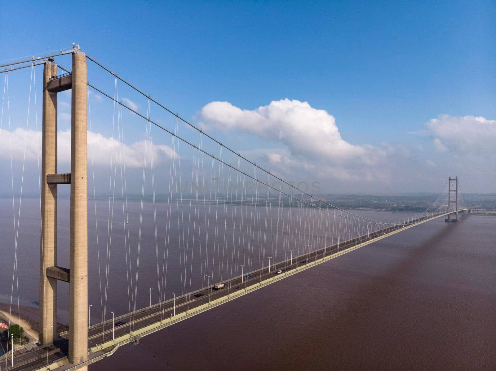 Aerial drone shot above the the Humber single-span suspension bridge (the longest in the world when it opened), against water with blue sky and cumulus clouds. Hessle, Hull, Yorkshire