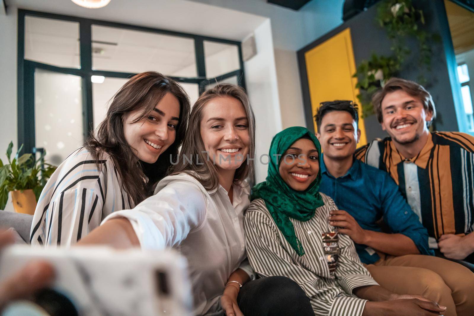 Group of business people during break from the work taking selfie picture while enjoying free time in relaxation area at modern open plan startup office. Selective focus by dotshock