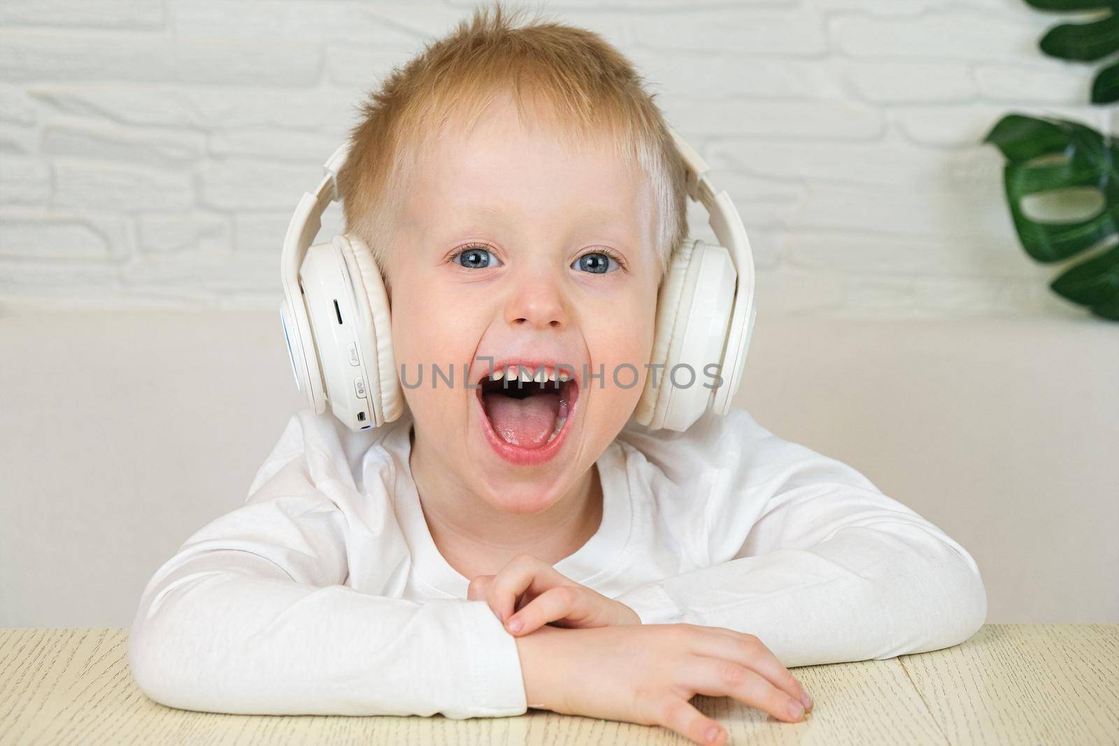 Little european boy smiles in a white t-shirt with big white headphones, listens to music and looks at the camera. Slow motion. The concept of music, home leisure. 4k. by chelmicky
