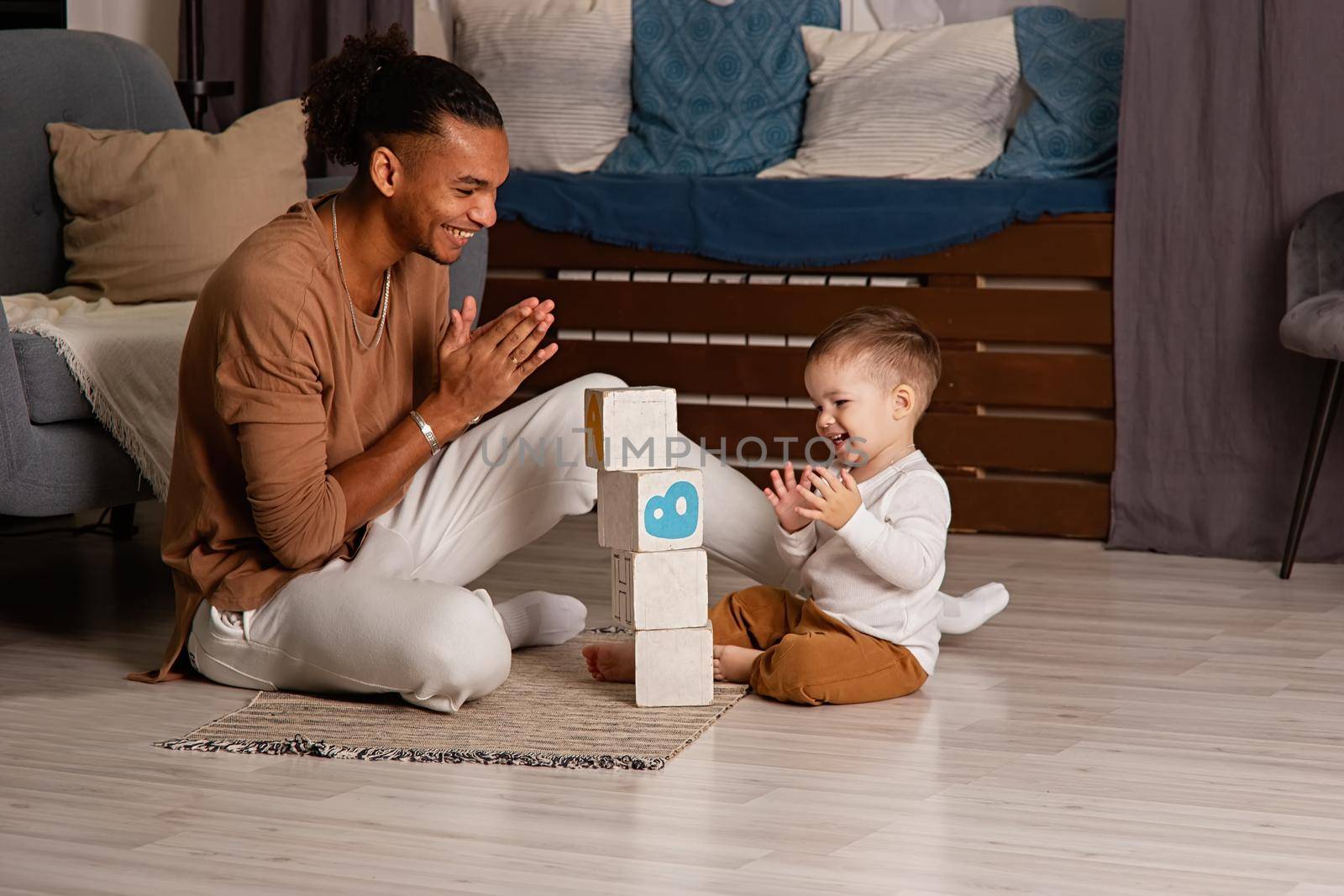 Young father and little son have fun playing cubes on the floor of the room, build a tower and rejoice