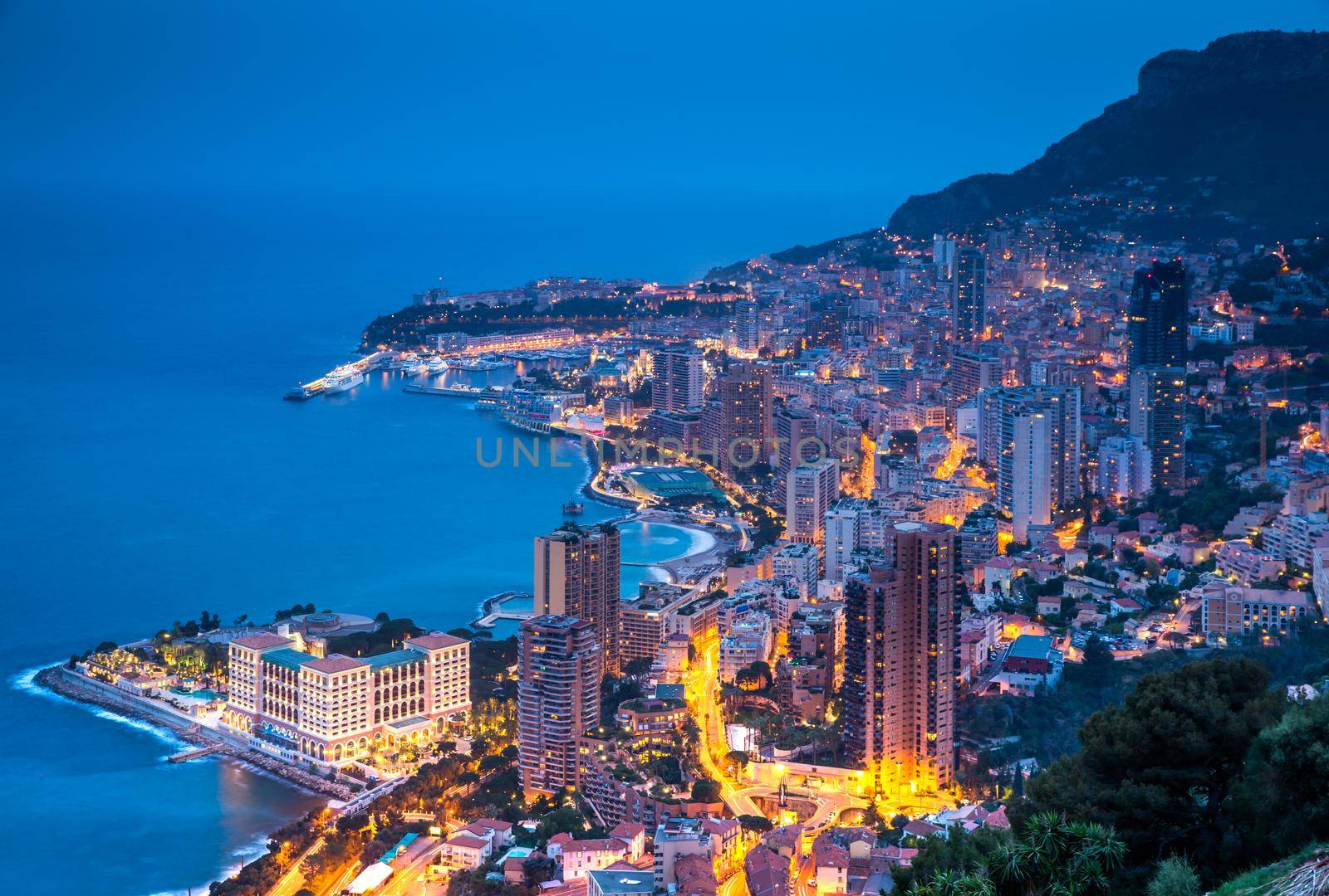 Aerial view of Monaco - Monte-Carlo at dusk, cityscape with night illumination, mountain, skyscrapers, mediterranean sea. High quality photo